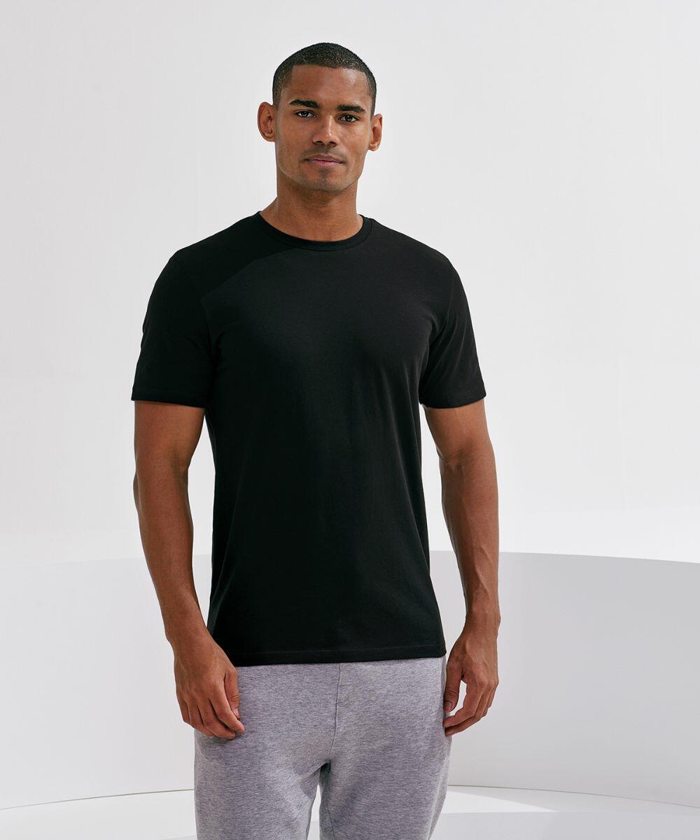 A person wearing a black Tri-Dri TR001 t-shirt and grey pants stands against a plain white background.