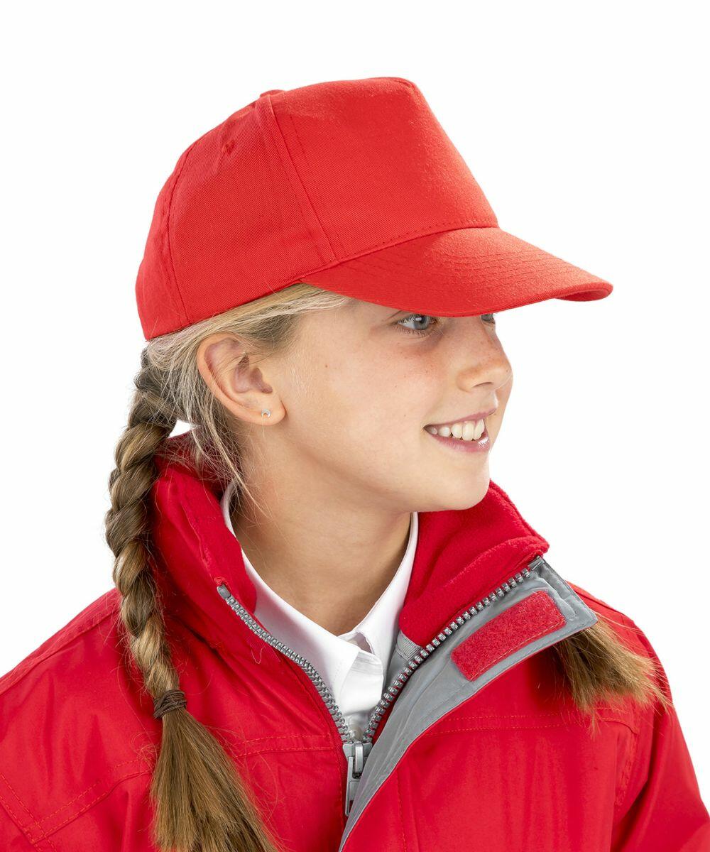A young girl wearing a red Result Genuine Recycled R984J baseball cap and red jacket with braided hair looking to the side and smiling.