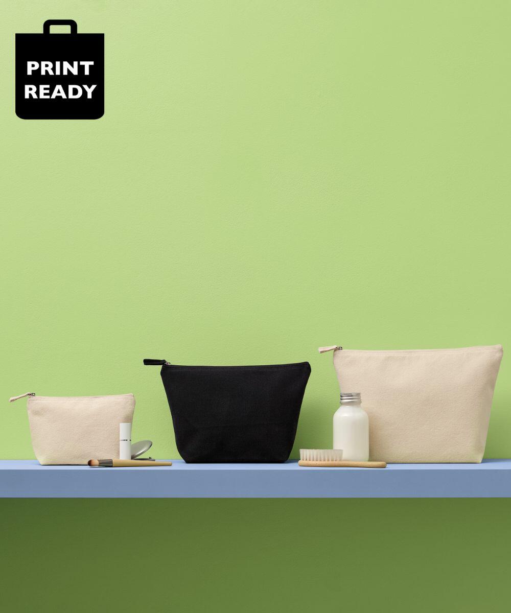 Three zippered pouches (small, medium, large) from Nutshell in the RL800 series in beige and black are displayed on a blue shelf with a toothbrush, lotion, and lipstick against a green background.