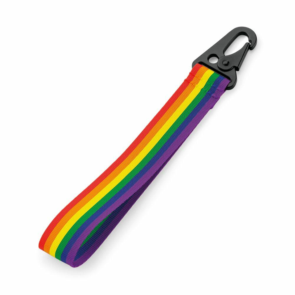 The Bagbase BG100 features a vibrant strap with a rainbow pattern and an attached black carabiner clip. The strap showcases stripes in purple, blue, green, yellow, orange, and red.
