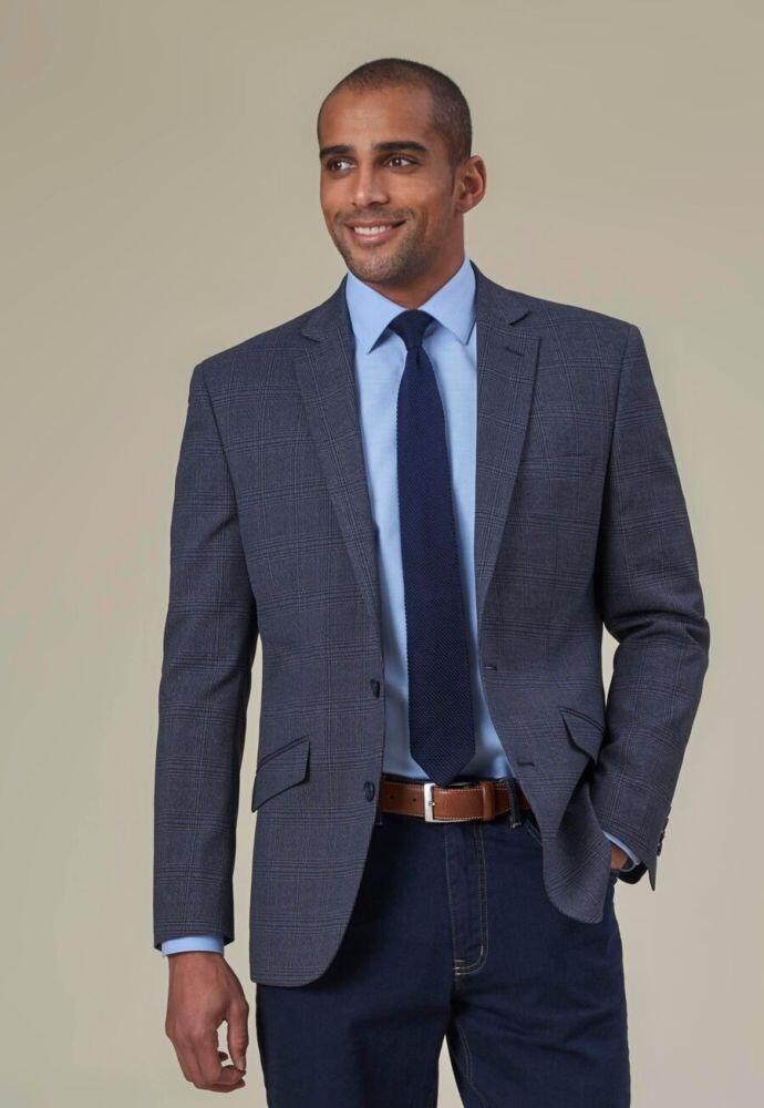Man wearing a Lucio Jacket from Brook Taverner over a blue shirt and tie, standing against a beige background, smiling.