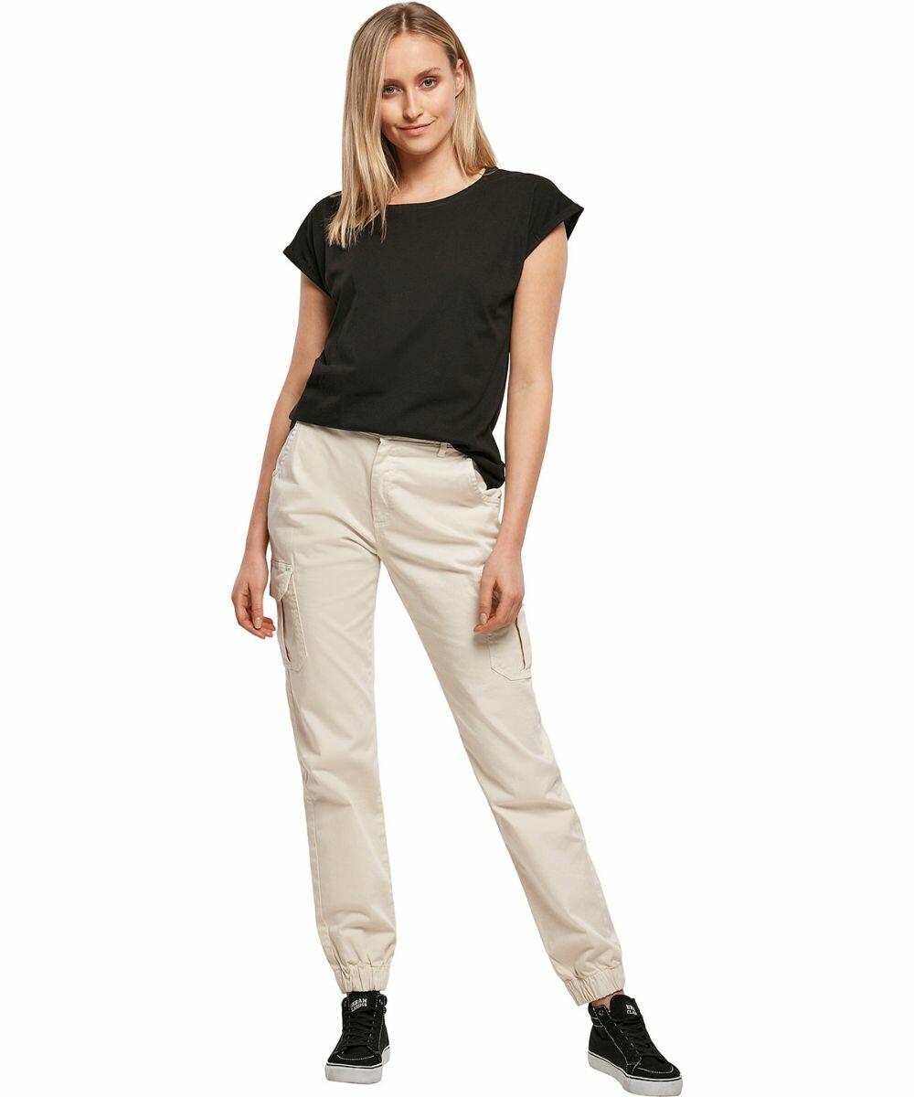 A person in a black BY092 t-shirt from Build Your Brand and beige cargo pants stands casually, with a slight smile, facing forward.