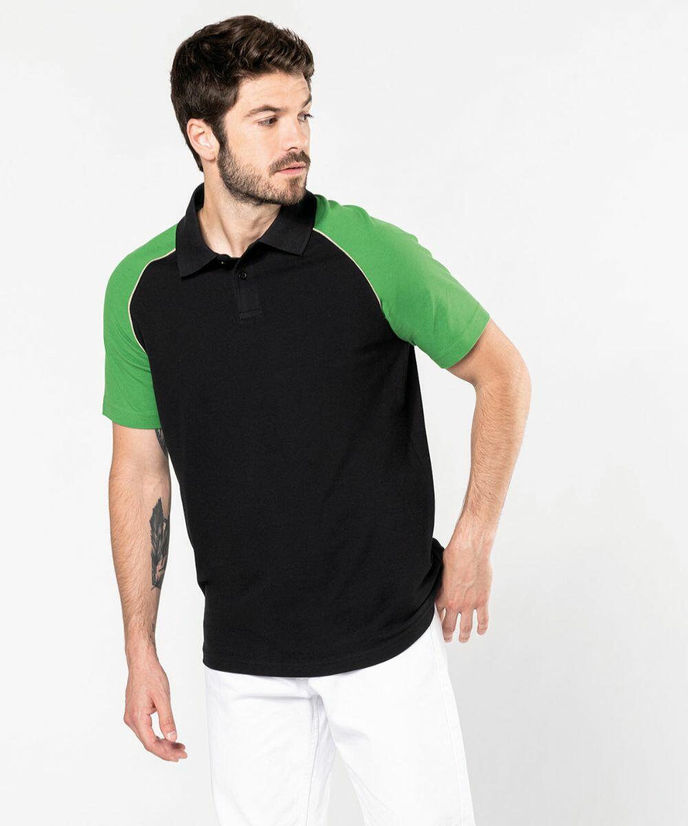 A man with short hair and a beard wears a black Kariban KB226 polo shirt with green sleeves and white pants. He has a tattoo on his right forearm and is looking to his left.