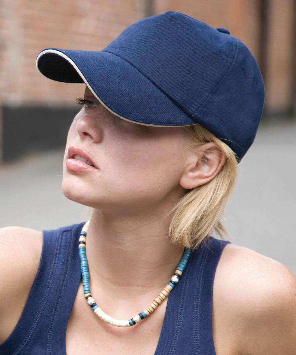 A person with short blond hair wearing a blue cap, navy RC50X tank top by Result, and a beaded necklace.