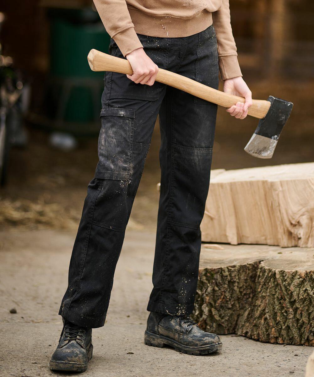 Person holding an RG235 from Regatta next to chopped wooden logs, wearing black pants and dusty boots, in an outdoor setting.