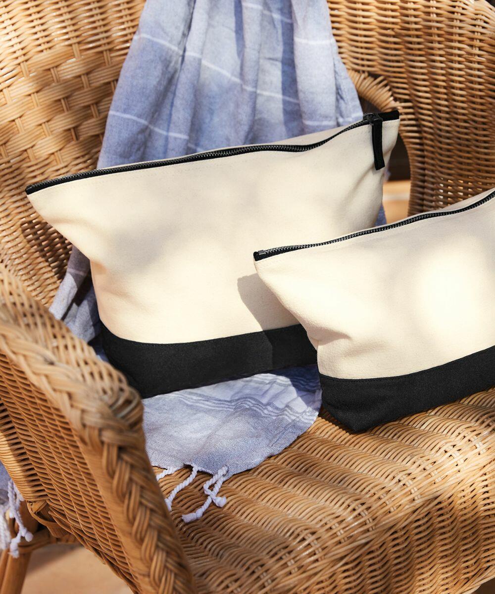 Two beige and black Westford Mill WM544 zippered pouches are placed on a wicker chair with a blue and white striped cloth draped over the back.