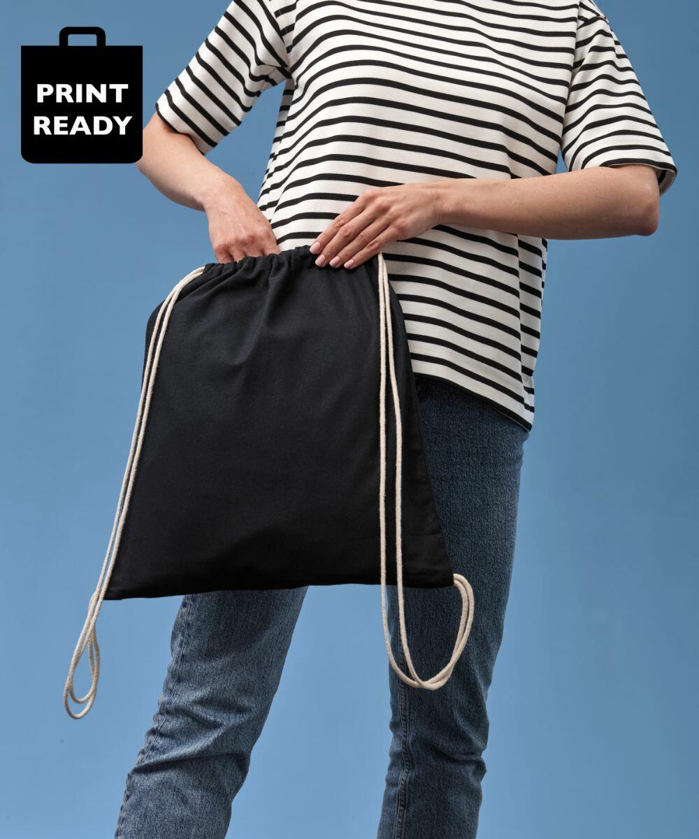 Person in striped shirt and jeans holding a black Nutshell RL300 with white cords against a blue background.
