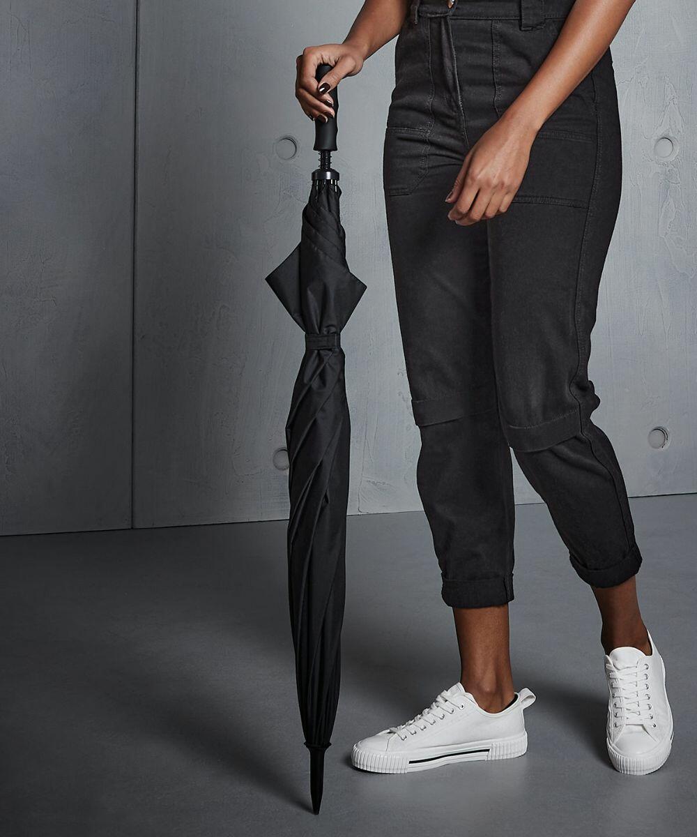 Person dressed in black pants and white sneakers holding a closed black Quadra QD360.