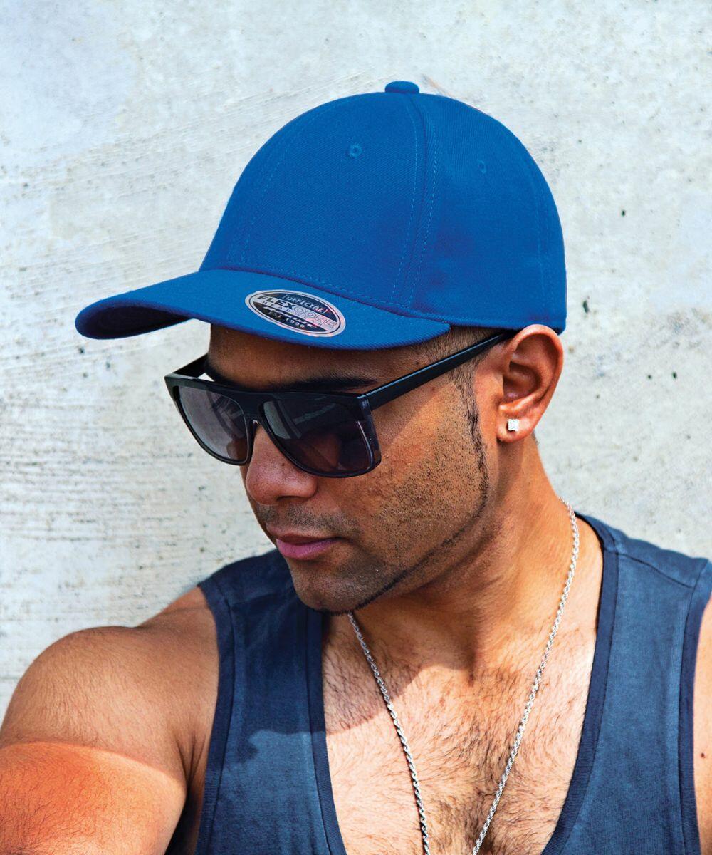 A man wearing a blue cap, RC85X sunglasses by Result, and a sleeveless black shirt, standing against a concrete background.