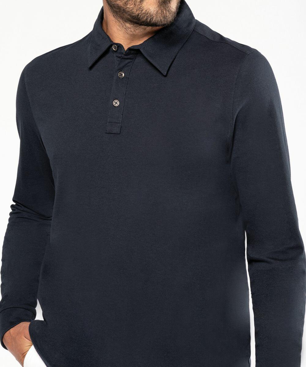 A person wearing a dark long-sleeve Kariban KB264 shirt with three buttons stands with one hand in their pocket. Only the upper torso and part of the face are visible.