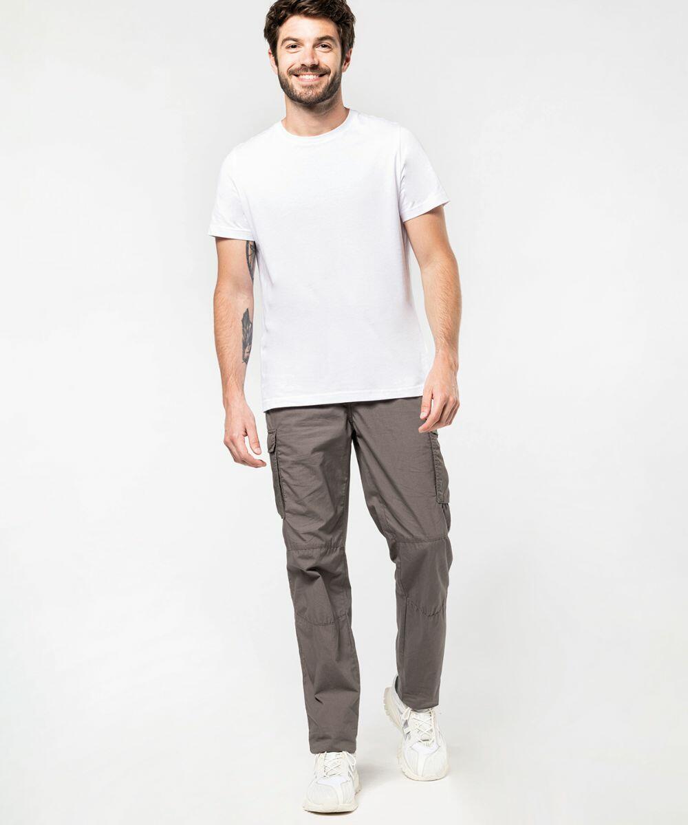 A man in a Kariban KB745 and grey cargo pants is smiling and walking forward against a plain white background.