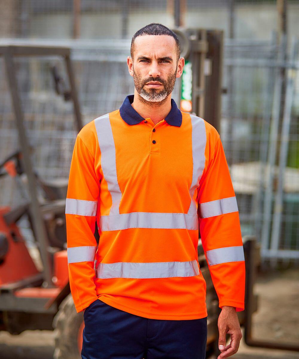 A man in a high-visibility orange RX715 safety shirt with reflective stripes from ProRTX stands in front of construction equipment.