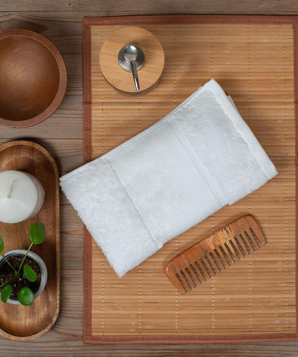 A neatly folded Towel City TC503, a wooden comb, a candle, a potted plant, wooden bowls, and a spoon rest on a bamboo mat and a wooden surface.