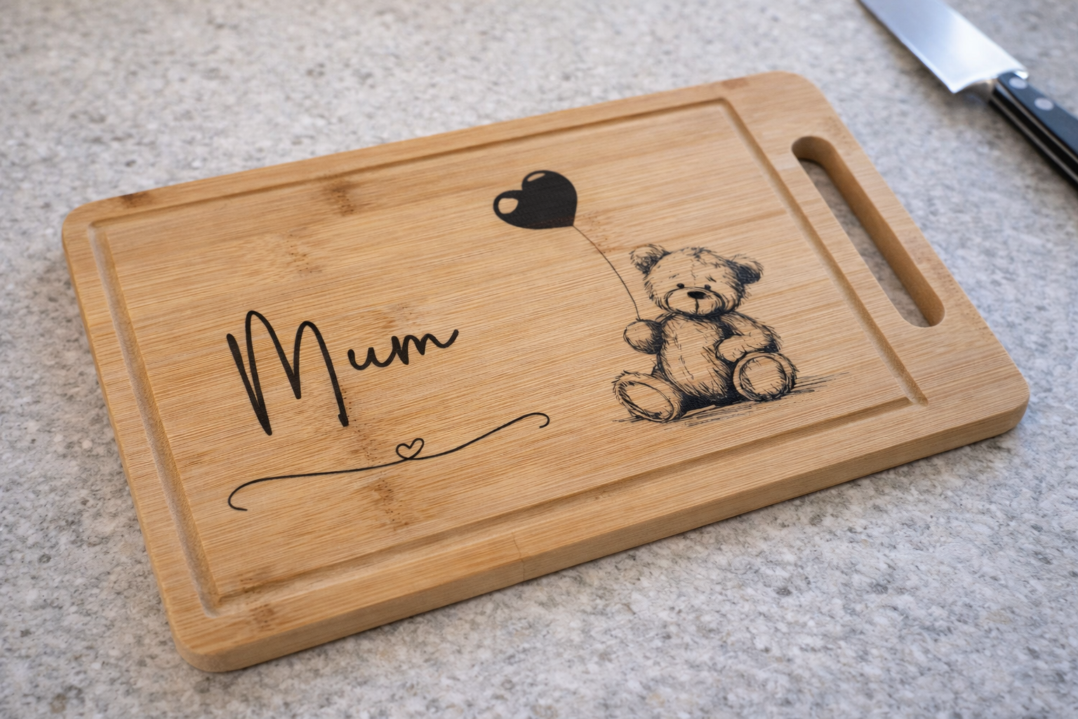Bamboo chopping board with a laser etched design of a cute scruffy ted holding a balloon and a tasteful "Mum" design on a kitchen worksurface