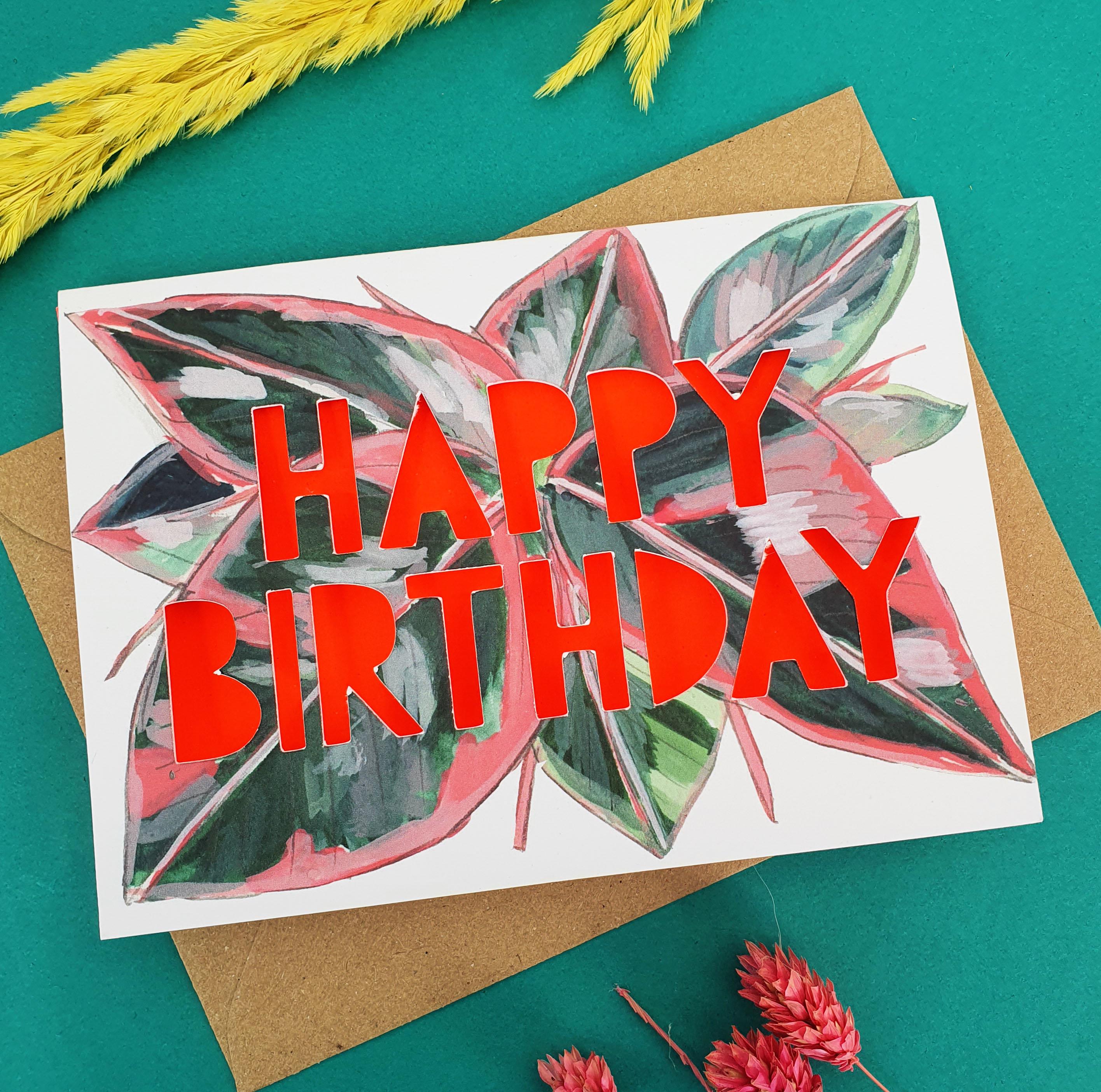 close up of Paper cut card with 'Happy Birthday' typography on a printed prayer plant 350 gsm card with neon coral liner.