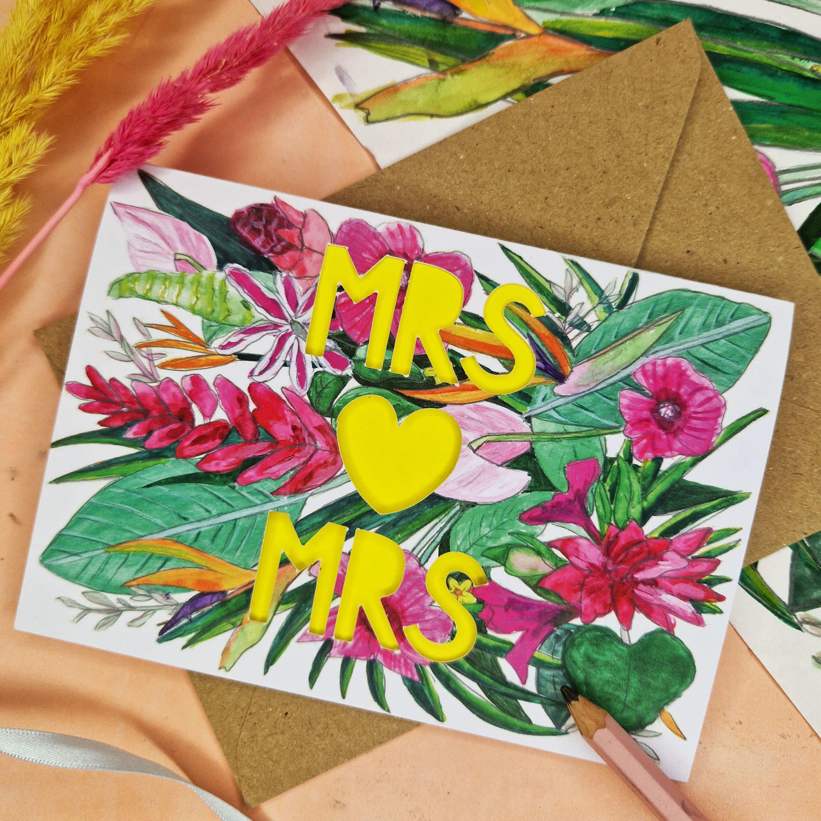 Flat lay of Floral Card with Paper cut text that says Mrs and Mrs with bright floral background.