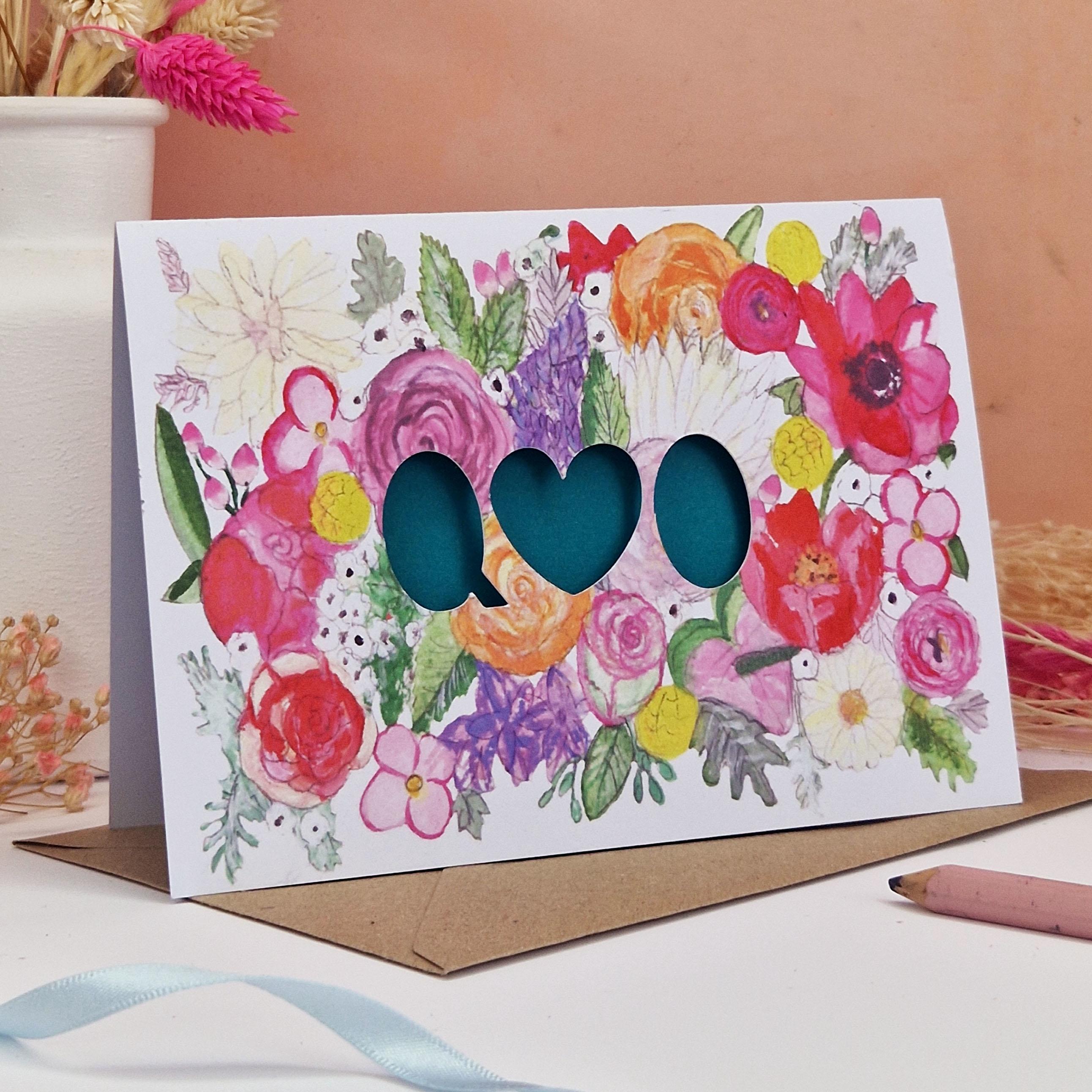 hand shot of Floral Card with Paper cut text that is personalised with Initials with bright floral background and turquiose paper liner inside.