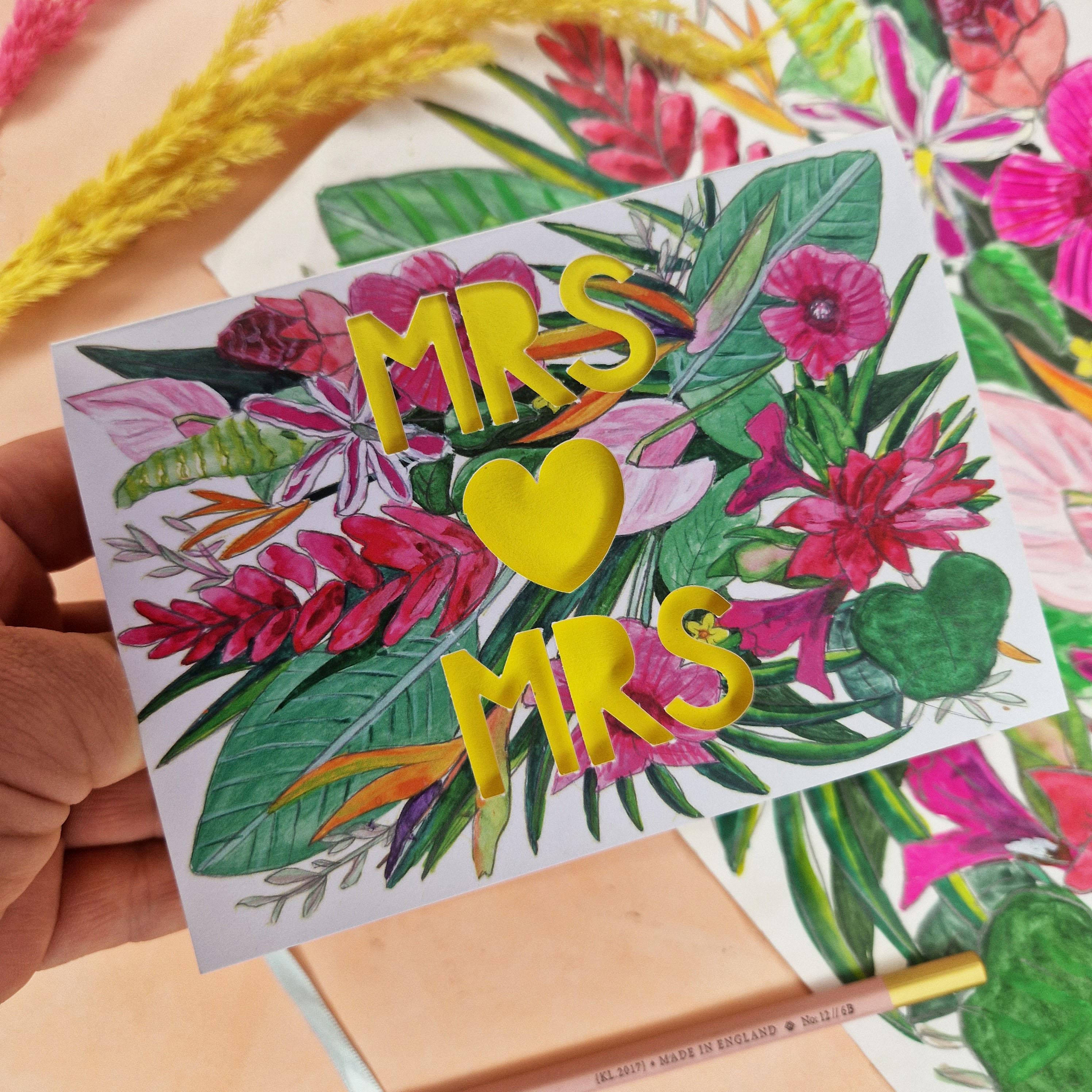 Hand shot of Floral Card with Paper cut text that says Mrs and Mrs with bright floral background.