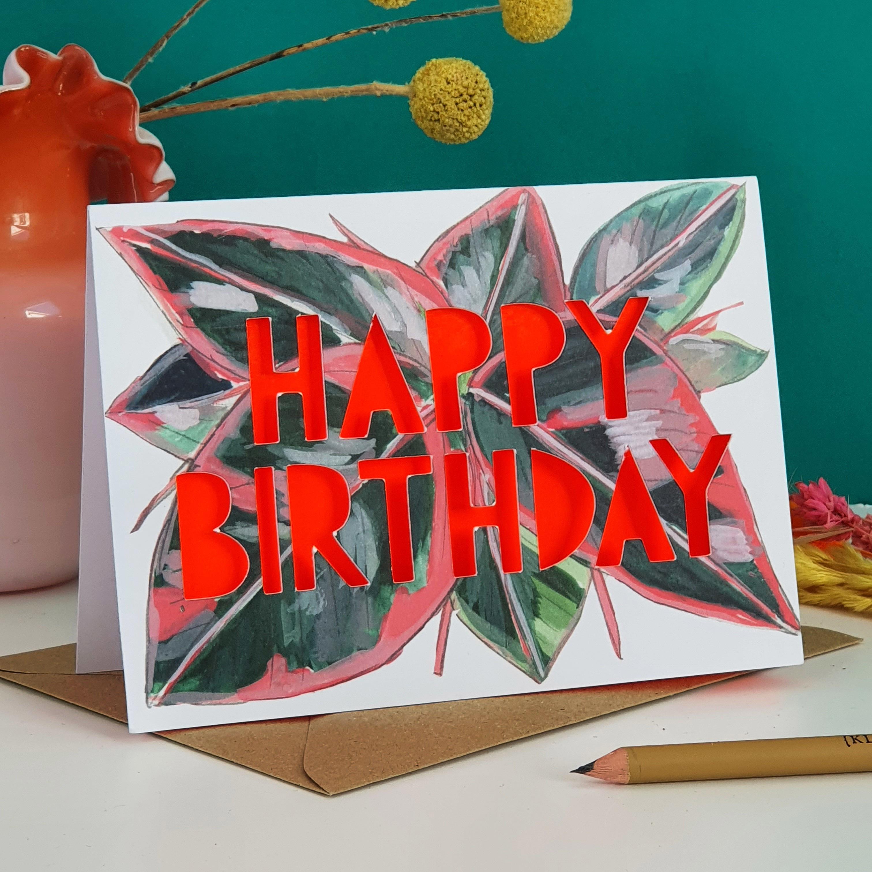 Paper cut card with 'Happy Birthday' typography on a printed prayer plant 350 gsm card with neon coral liner.
