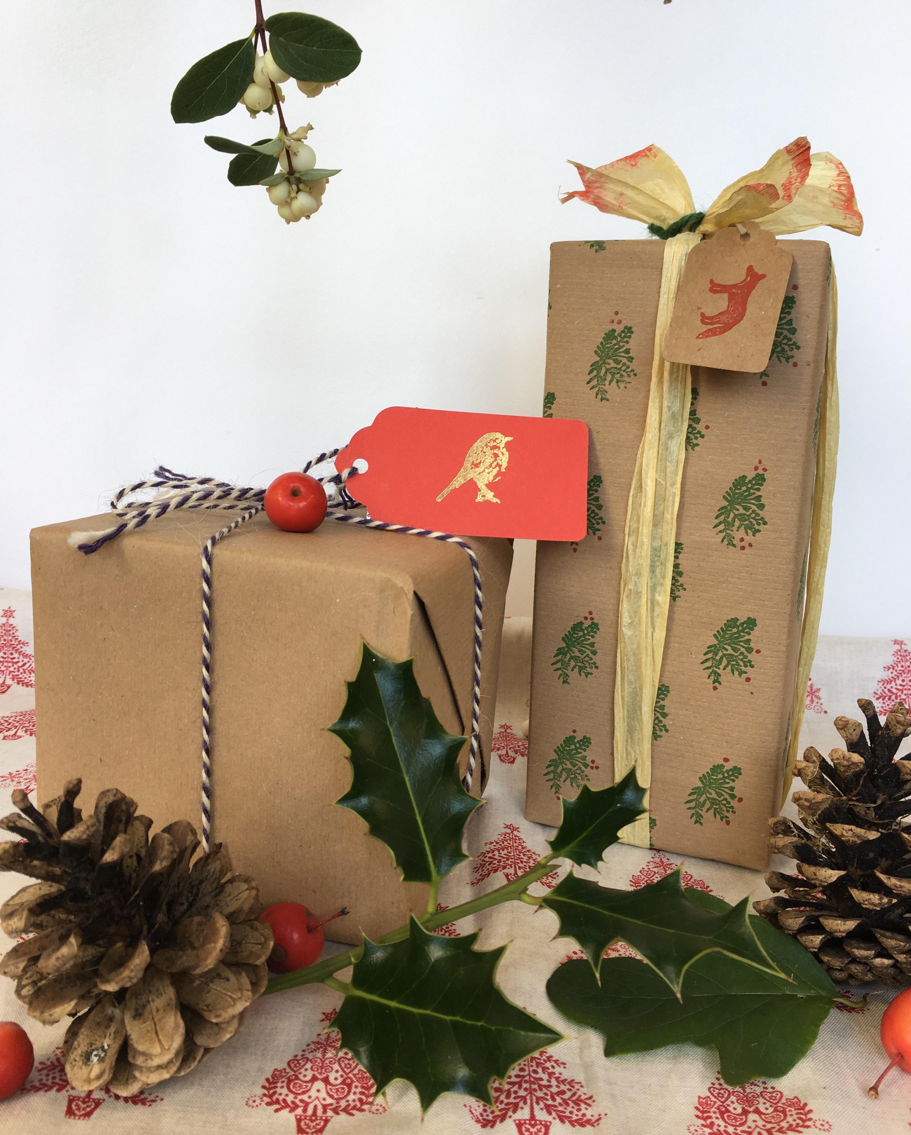 Image shows to boxes wrapped with kraft paper and decorated with string, ribbons and natural items such as holly and pines