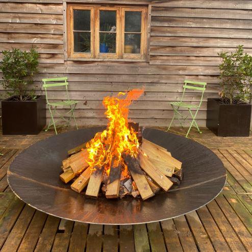 large corten steel fire bowl with flaming logs at night