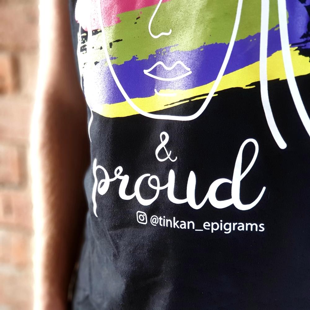 Close up photo of black t-shirt with white handdrawn face and rainbow painted stripes with the words I'm Me & Proud printed. Designed by thetinkan. VIEW PRODUCT >>