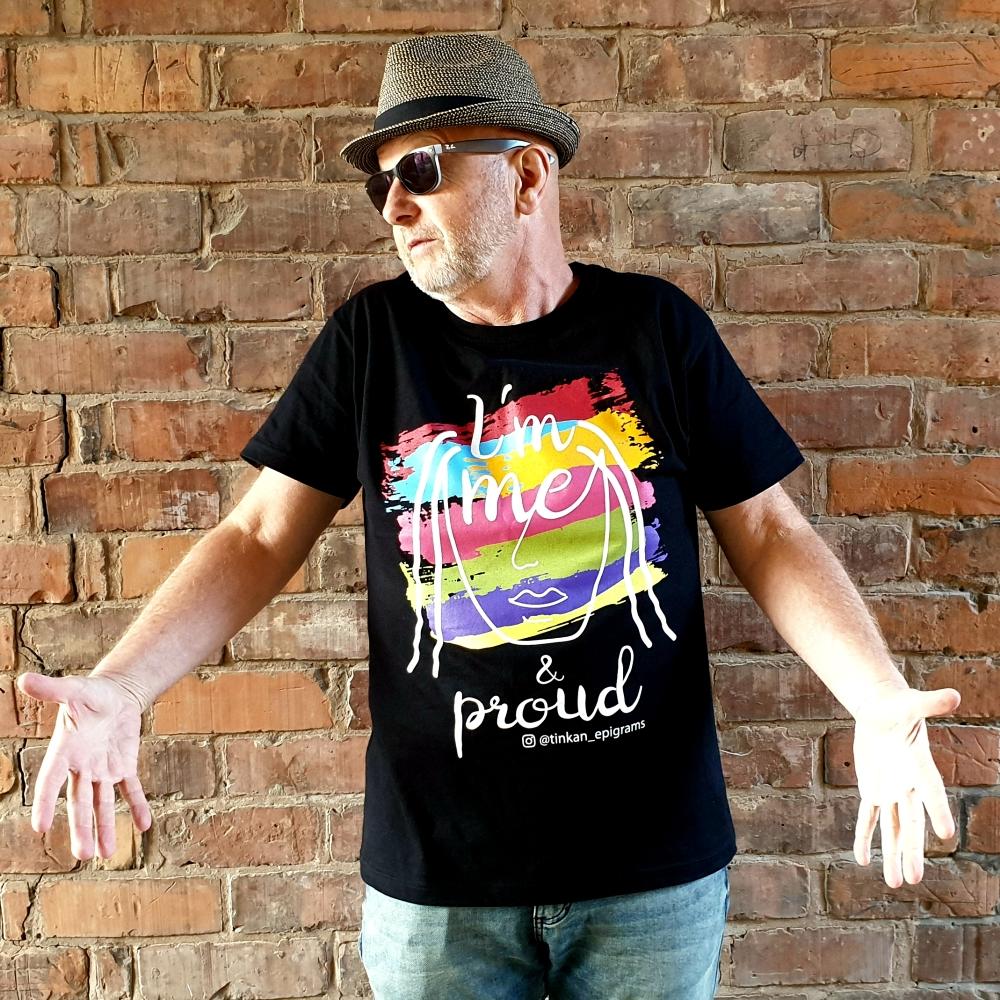 Adult male wearing black t-shirt with white handdrawn face and rainbow painted stripes with the words I'm Me & Proud printed. Designed by thetinkan. VIEW PRODUCT >>