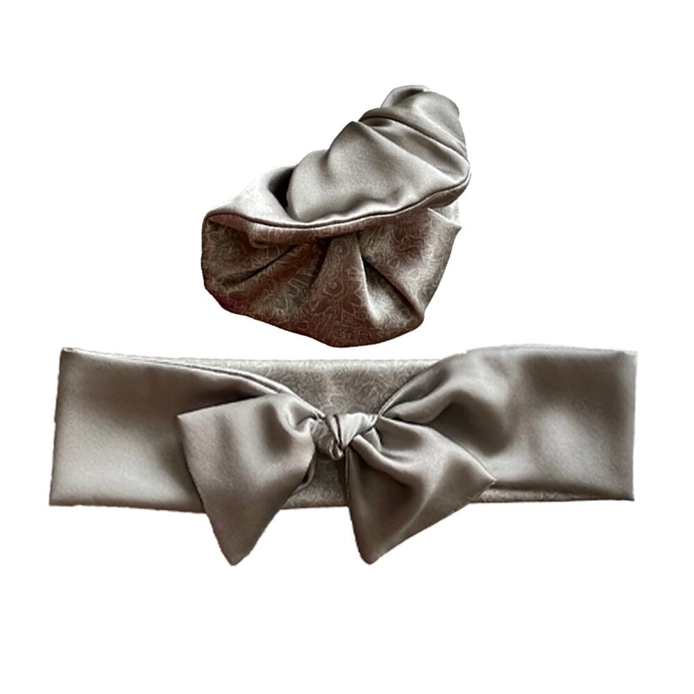 Soft grey coloured adjustable and reversible silk headband and scrunchie luxury gift set made from 95% silk satin and 5% elastane, stretching to fit comfortably. The headband is knotted to form a bow shape and the scrunchie is large (7 cm deep). Both are made with a signature silver-grey patterned silk satin print on the reverse.