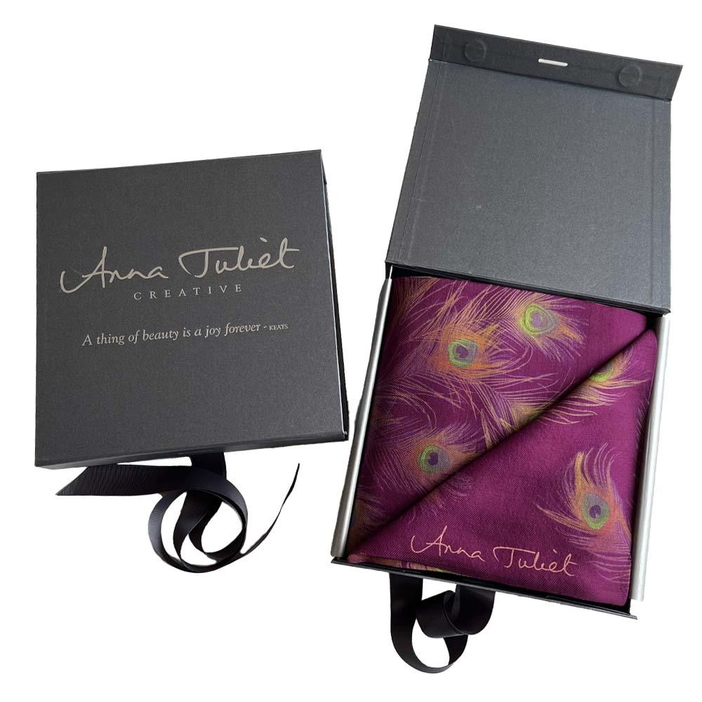 Gift boxed ready for the holiday season this purple-red mulberry coloured neck scarf is delicately wrapped in silver tissue and folded to show the peacock feather design when the box is opened.