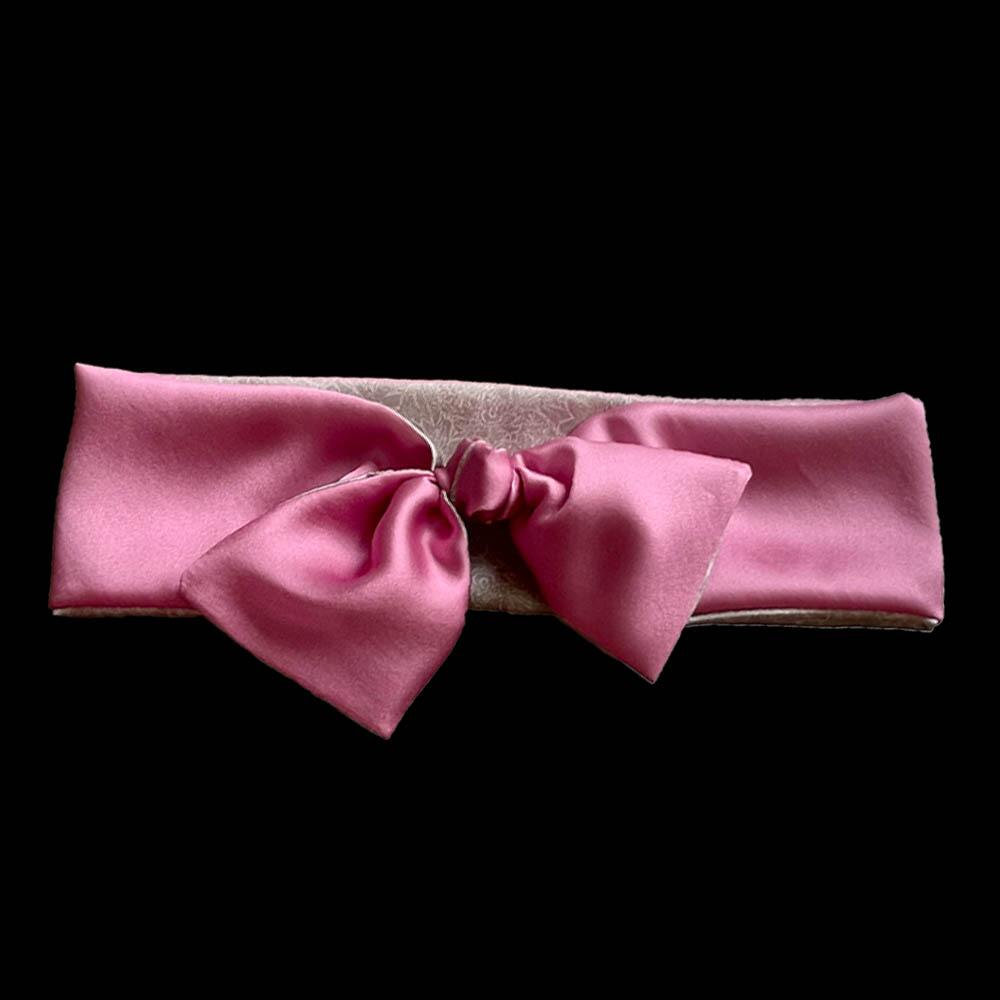 Rose pink coloured adjustable and reversible silk headband made from 95% silk and 5% elastane. The headband is knotted to form a bow shape and made with a signature silver-grey patterned silk satin print lining.