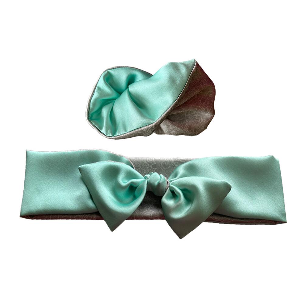 Aquamarine pale blue-green coloured adjustable and reversible silk headband and scrunchie luxury gift set made from 95% silk satin and 5% elastane, stretching to fit comfortably. The headband is knotted to form a bow shape and the scrunchie is large (7 cm deep). Both are made with a signature silver-grey patterned silk satin print on the reverse.