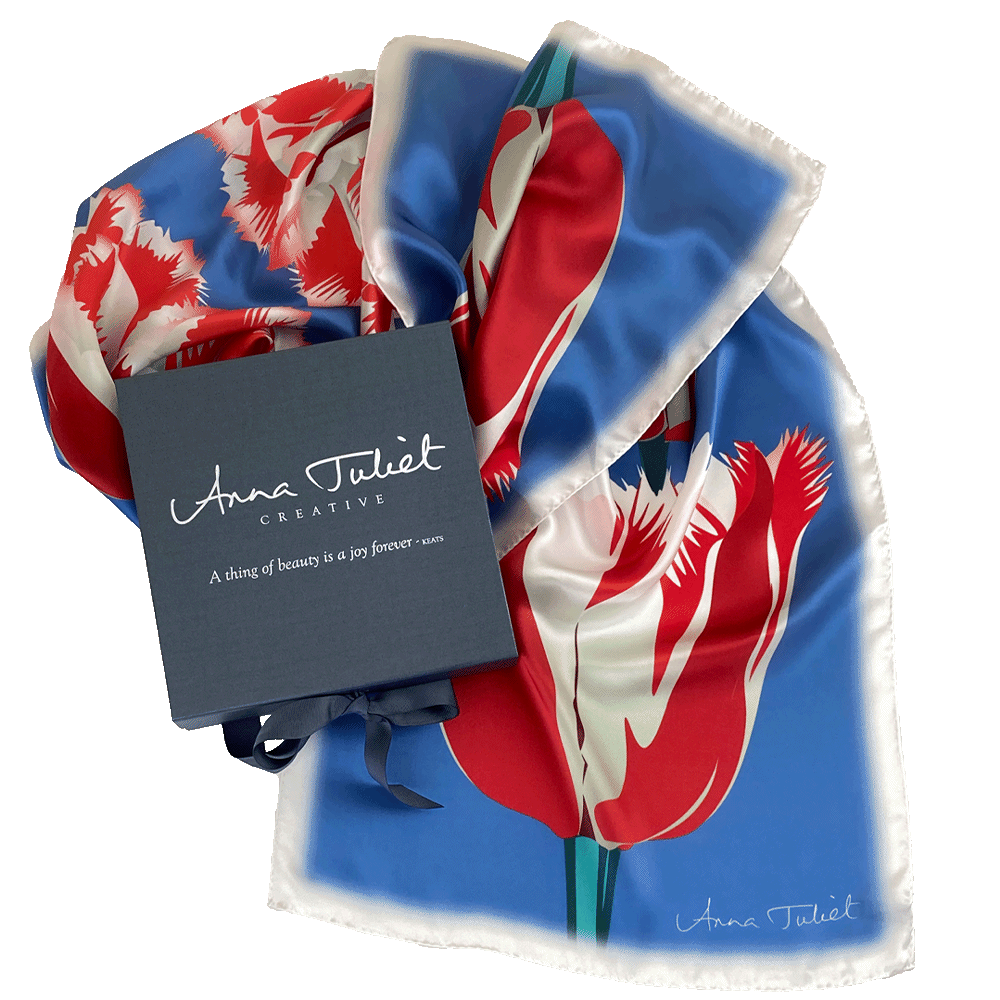 Floral pure silk scarf draped around a branded pewter-coloured gift box. Red and White Tulip on Blue by Anna Juliet Creative. Limited edition luxury silk scarf made in Britain.