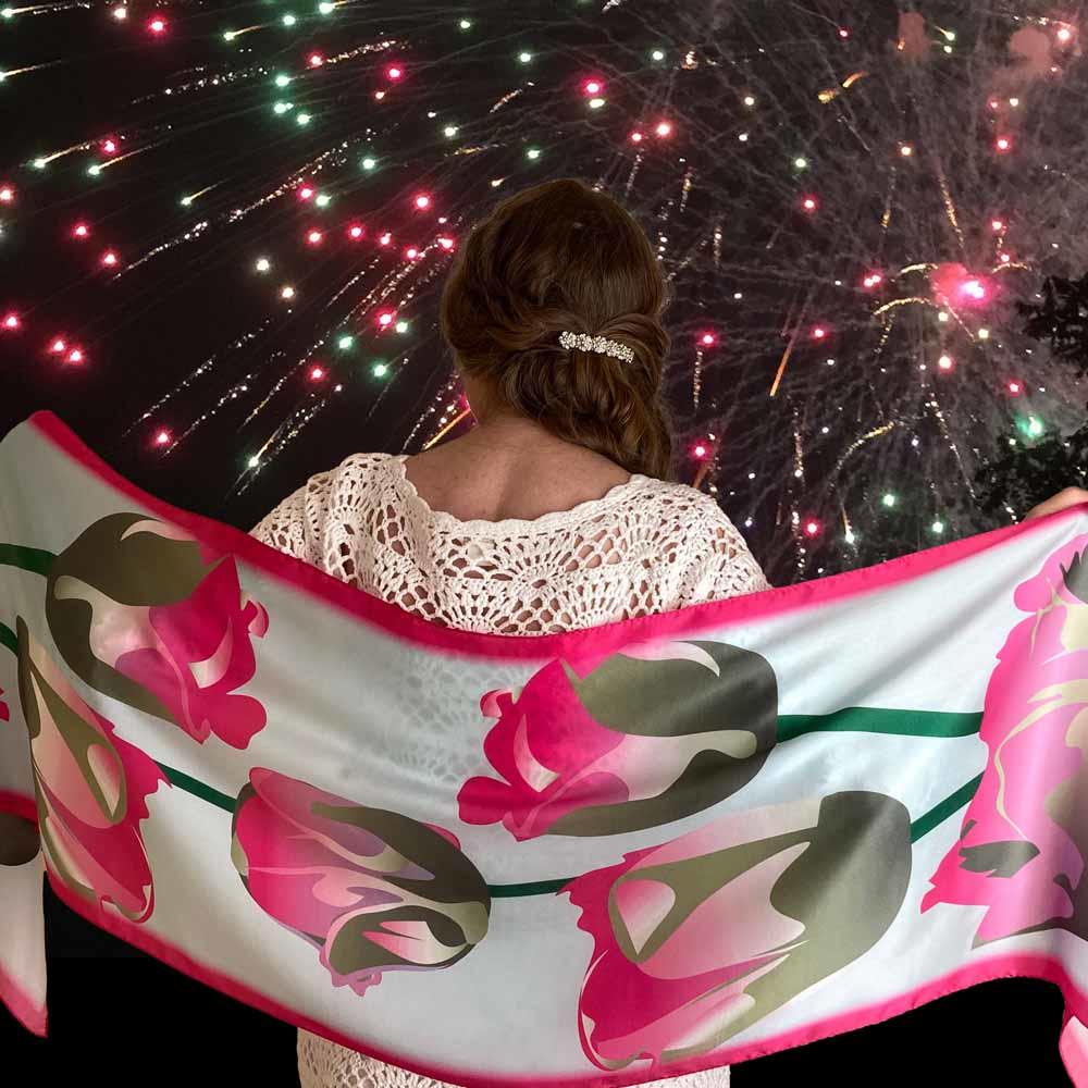 The artist is facing away from the viewer and is wearing a hot pink limited edition silk scarf across her shoulders. Pink fireworks can be seen in the background.