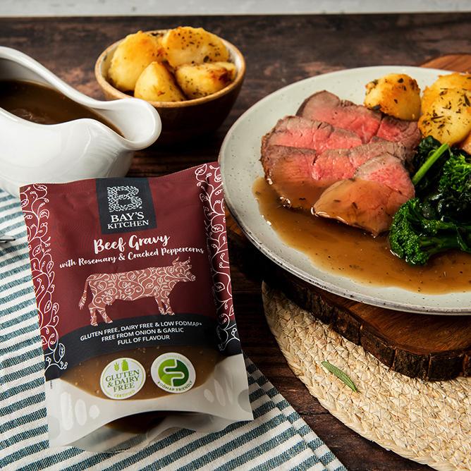 A packet of Bay's Kitchen Beef Gravy beside a plate of roast beef and vegetables