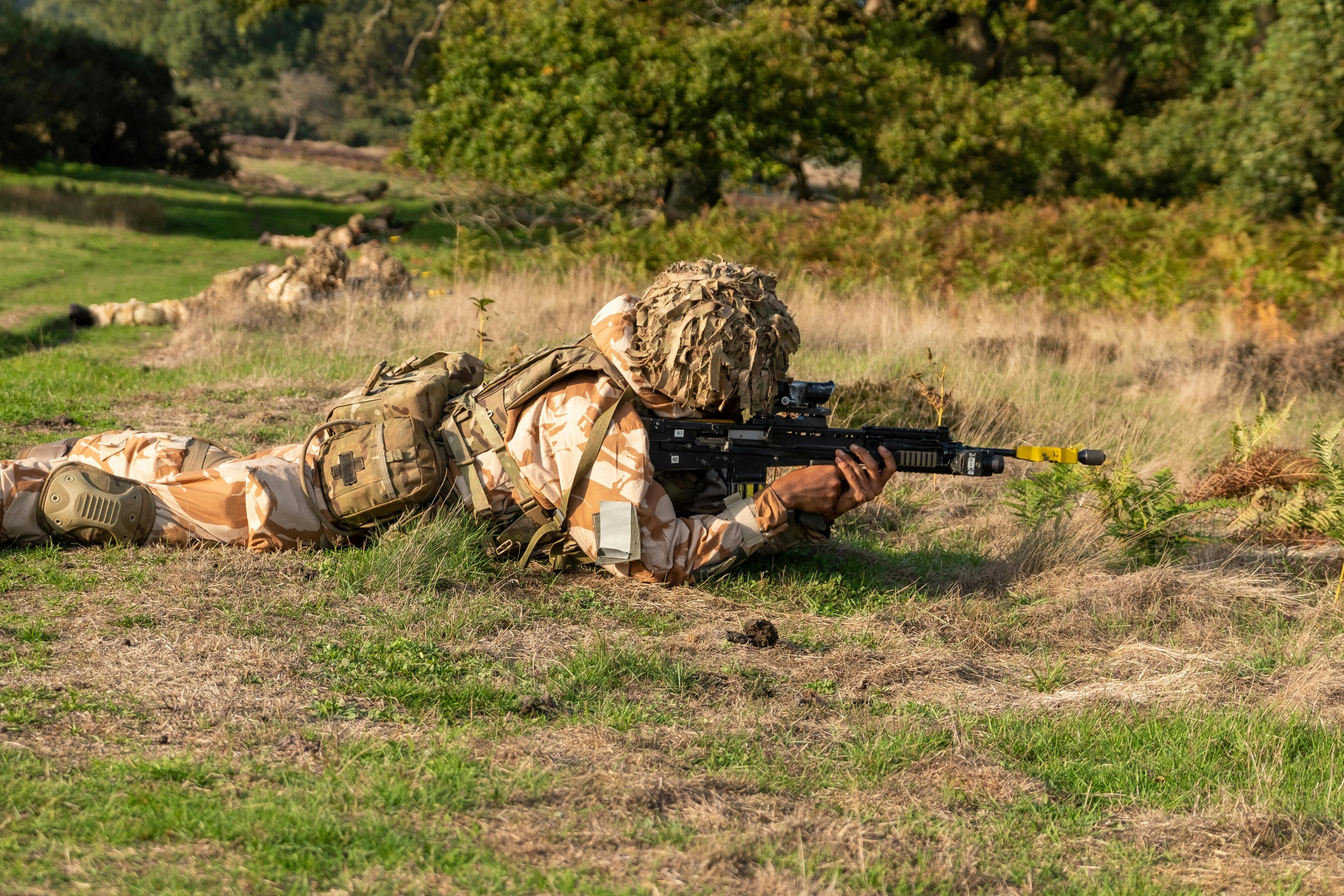 A Soldier Holding Rifle while Crawling on Grass Field