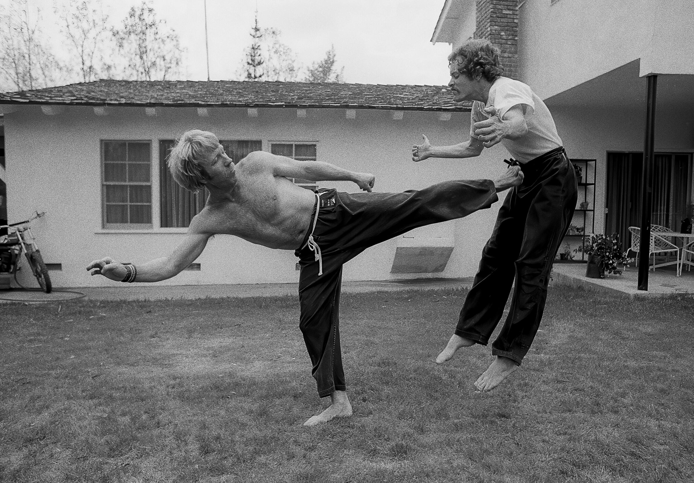 Martial arts master Chuck Norris demonstrating a signature Tang Soo Do power side kick during a training session in the backyard of his house in Palos Verdes, Los Angeles, in 1978. The kick has lifted his opponent off the ground.