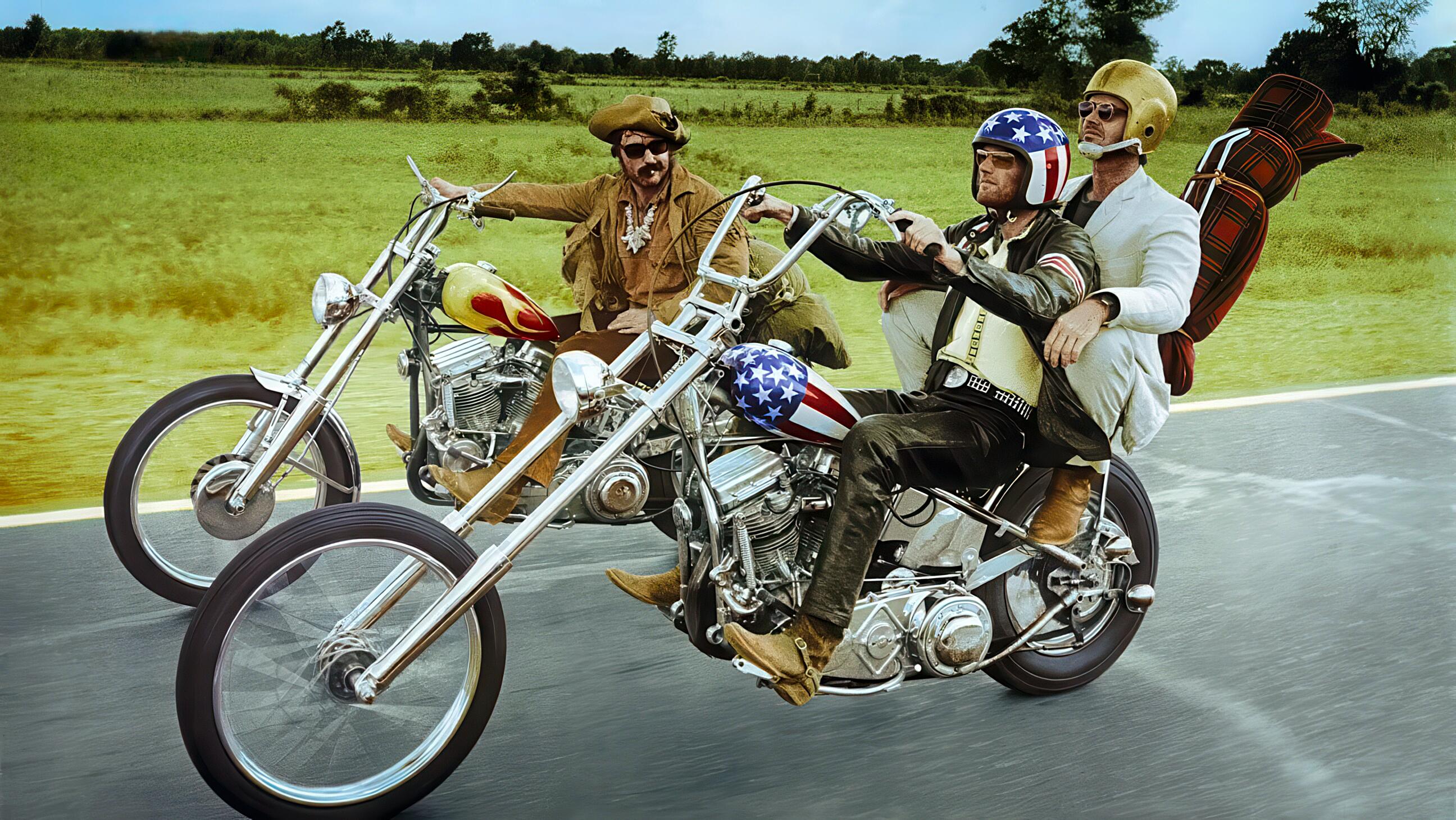 Peter Fonda, Jack Nicholson and Dennis Hopper riding along the road, side by side, in an iconic image from Easy Rider (1969). Peter Fonda as Wyatt ("Captain America") is riding a 1969 Harley-Davidson FLH Hydra-Glide (heavily customized chopper). Dennis Hopper as Billy is also riding a Harley-Davidson FLH but with different customisation. The film and its iconic motorcycles represent freedom, rebellion, and the counterculture spirit of the 1960s. The bikes were built by Cliff Vaughs and Ben Hardy, two African American custom bike builders from Los Angeles.