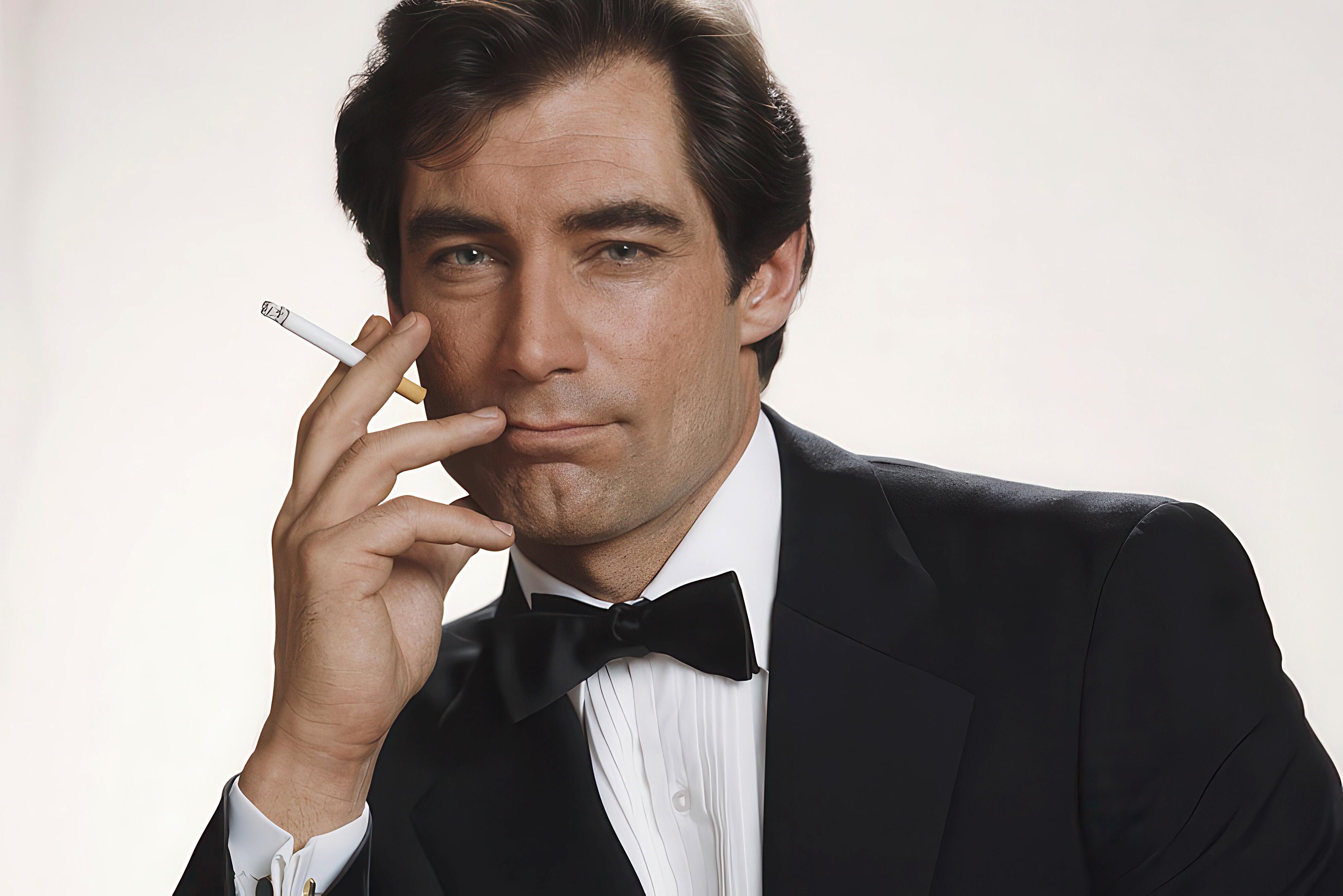 British actor, Timothy Dalton, posing in a black tuxedo, white dress shirt and cigarette for a famous publicity shot for The Living Daylights, released in 1987.