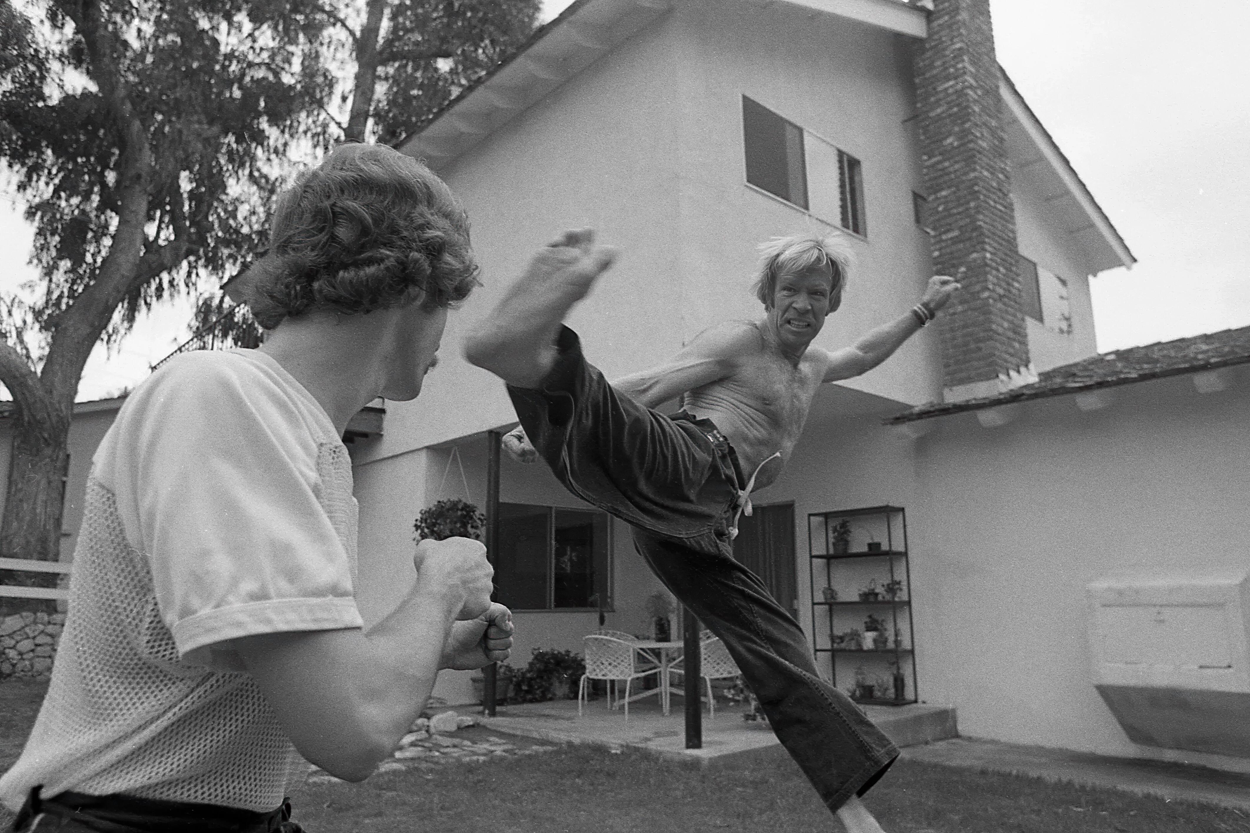 Martial arts world champion, Chuck Norris, performing a jumping kick to the head of a sparring-partner in the backyard of his house in Palos Verdes, Los Angeles in 1978.