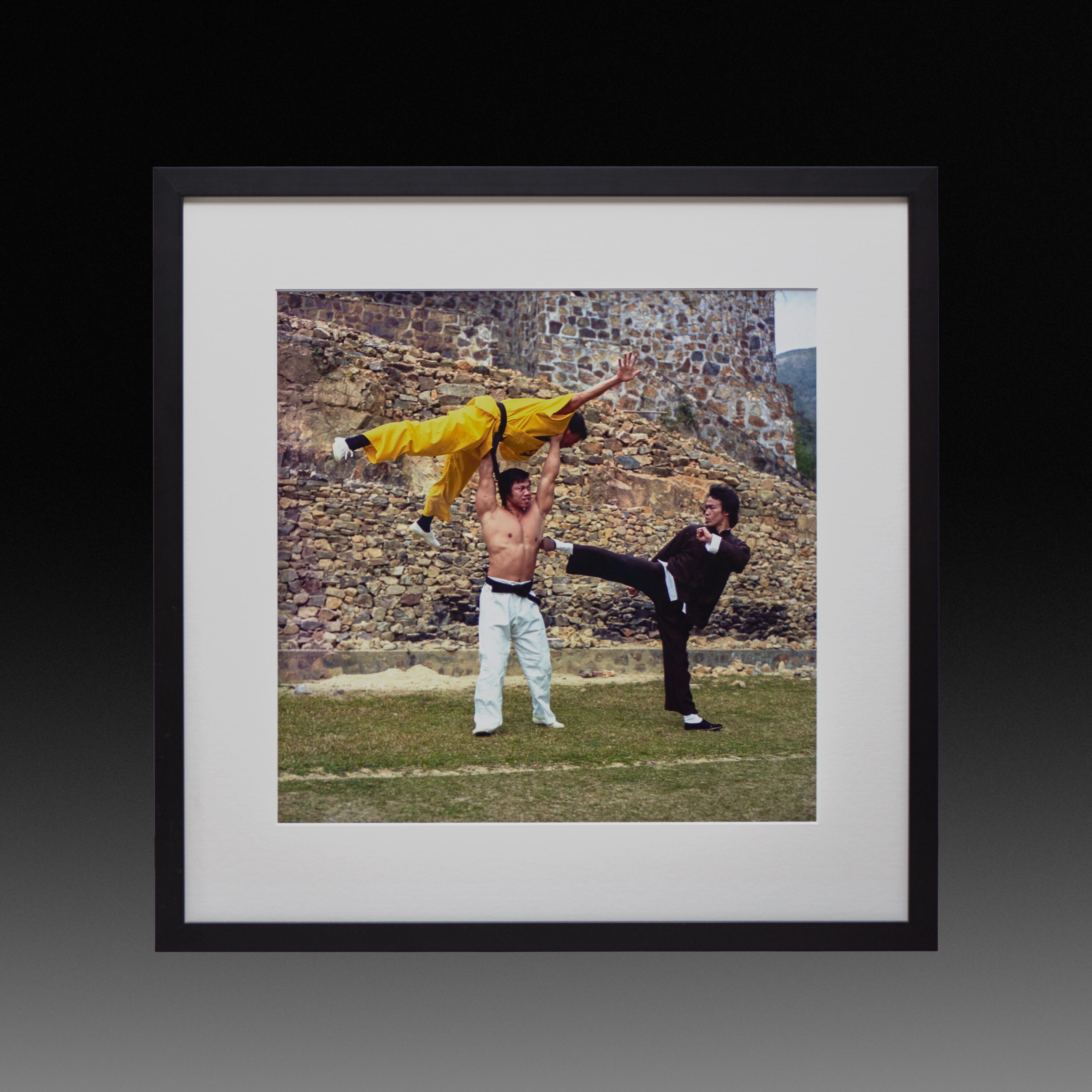 Framed exhibition print of Bruce Lee simulating a fight with Bolo Yeung, who holds Wu Ngan overhead; 1973 photoshoot.