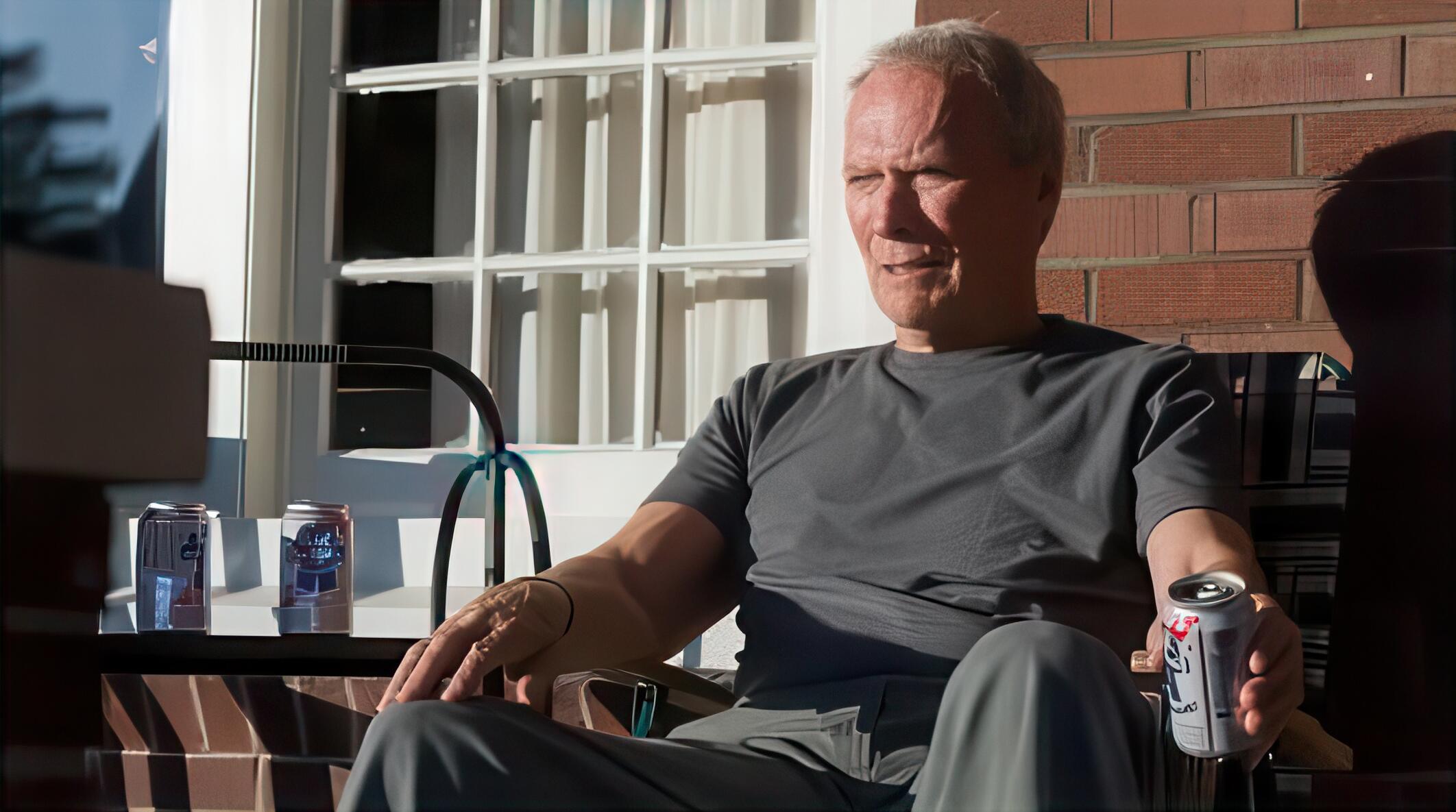 Still image captured from Gran Torino, featuring Clint Eastwood sat outside drinking from a can 