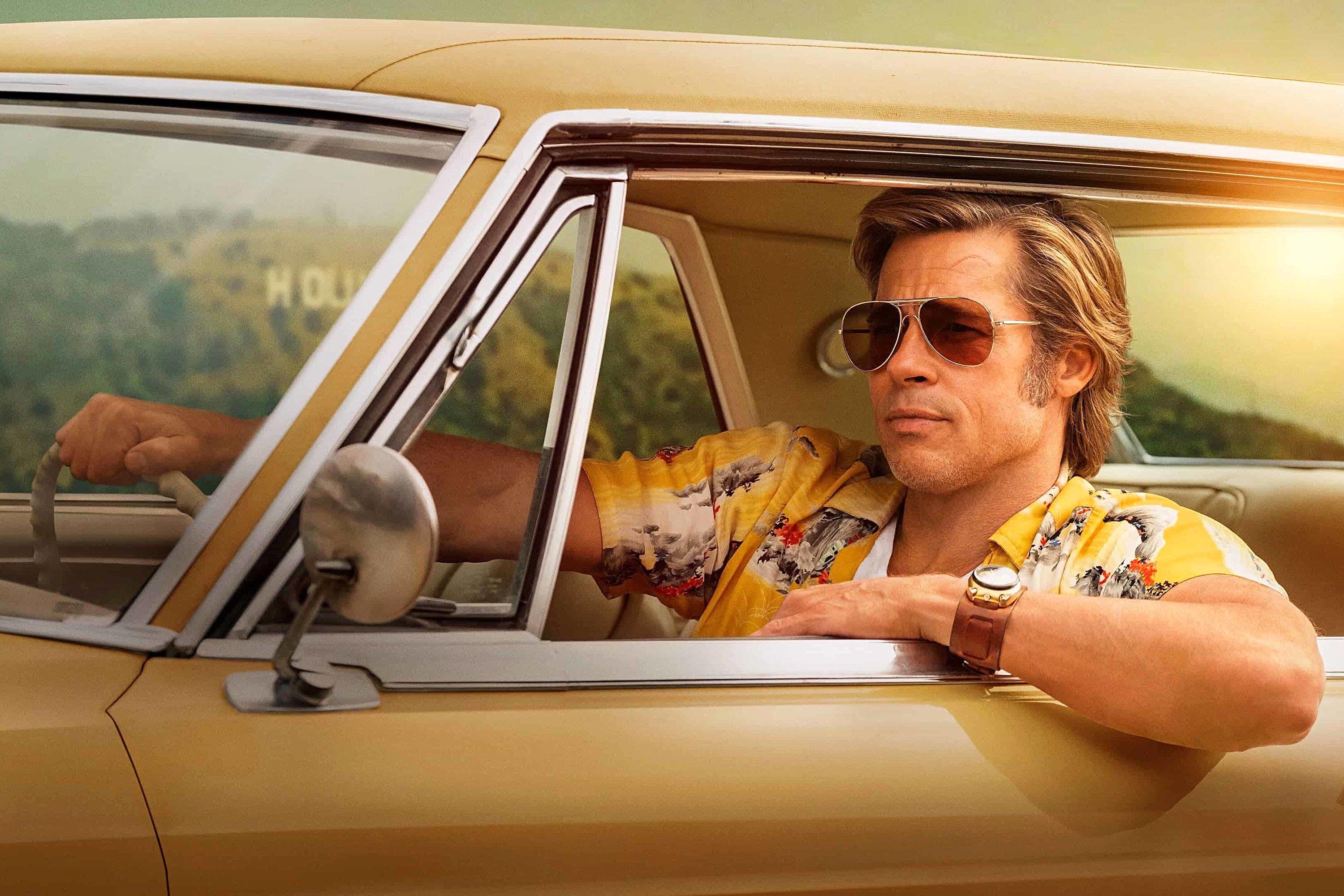 Brad Pitt, as Cliff Booth, posing in an unbuttoned yellow Aloha shirt worn over a faded Champion T-shirt—a nod to the classic American brand best known for spark plugs since its founding in 1908 – for Quentin Tarantino’s Once Upon a Time in Hollywood (2019). Pitt is wearing Oliver Peoples “OV 5217S” sunglasses, also known as the Oliver Peoples “Finley Vintage Sun.” He is driving a 1966 Cadillac Coupe DeVille in ‘Cape Ivory’ yellow.