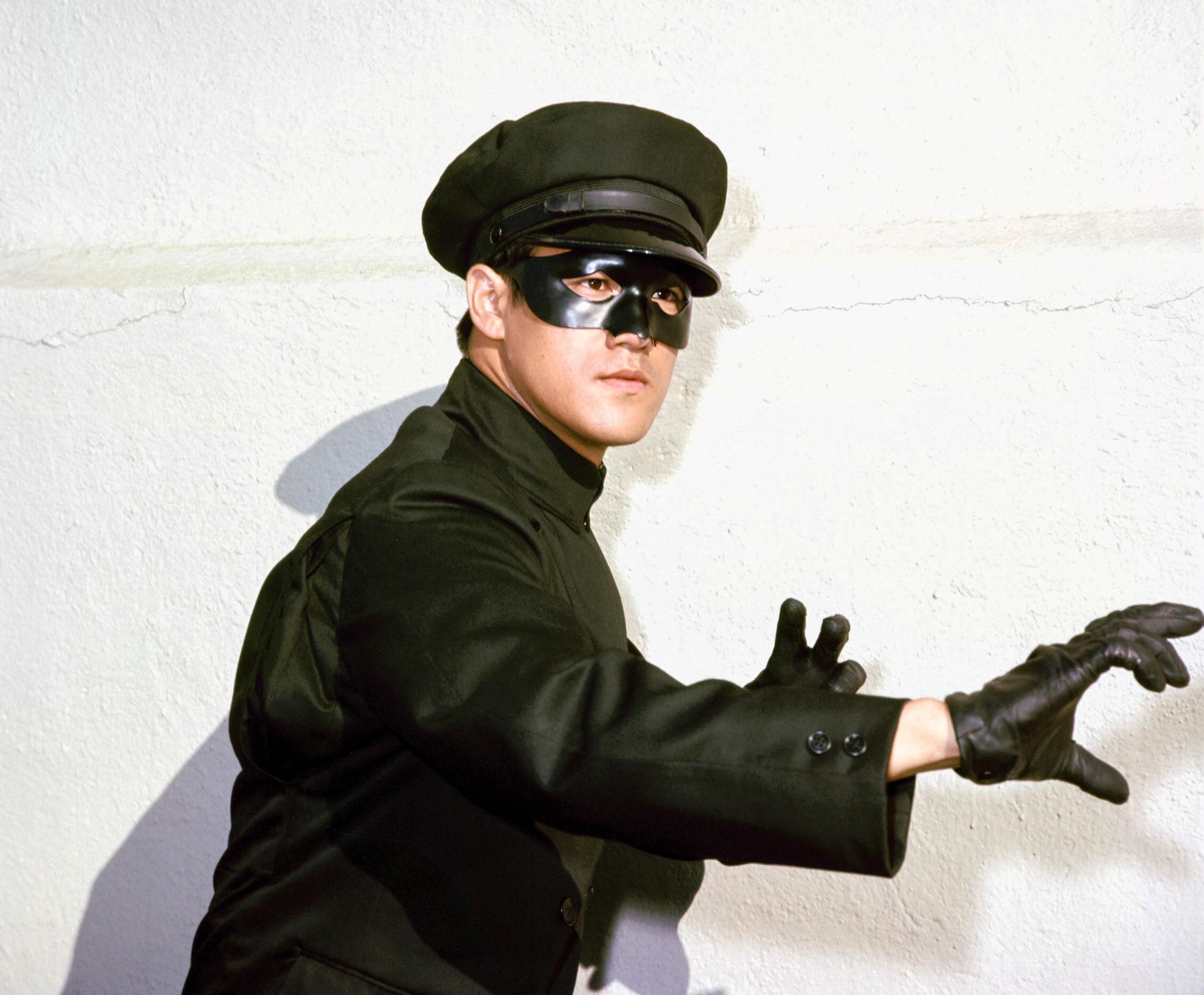 Bruce Lee as Kato in The Green Hornet TV series, posing in a kung fu stance wearing his black mask and chauffeur uniform.