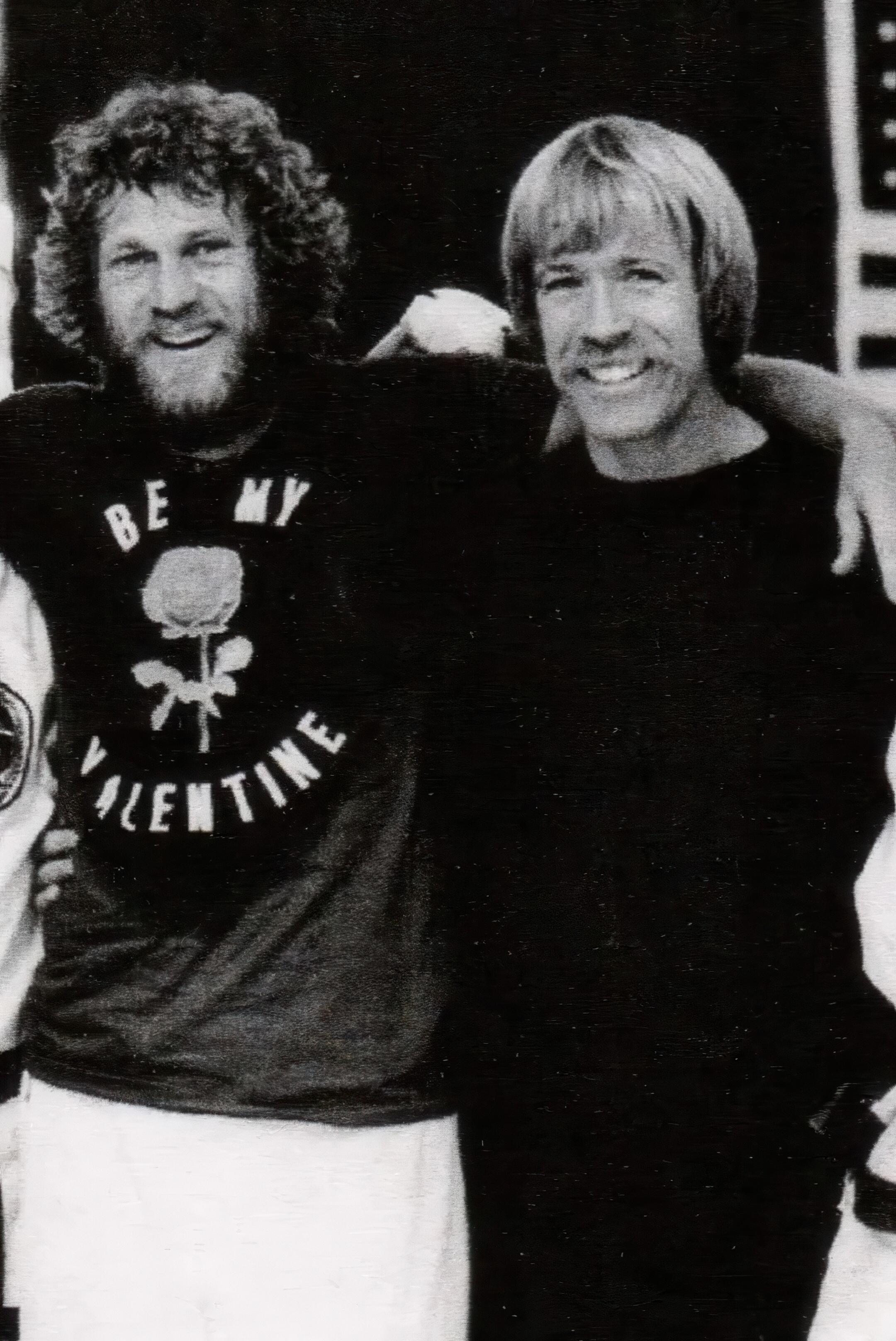 Steve McQueen and Chuck Norris with their arms around each other during 1970s martial arts training session, reflecting McQueen’s close friendship with Norris, whom he studied under, and echoing the similarly tight bond he shared with fellow martial arts legend Bruce Lee.