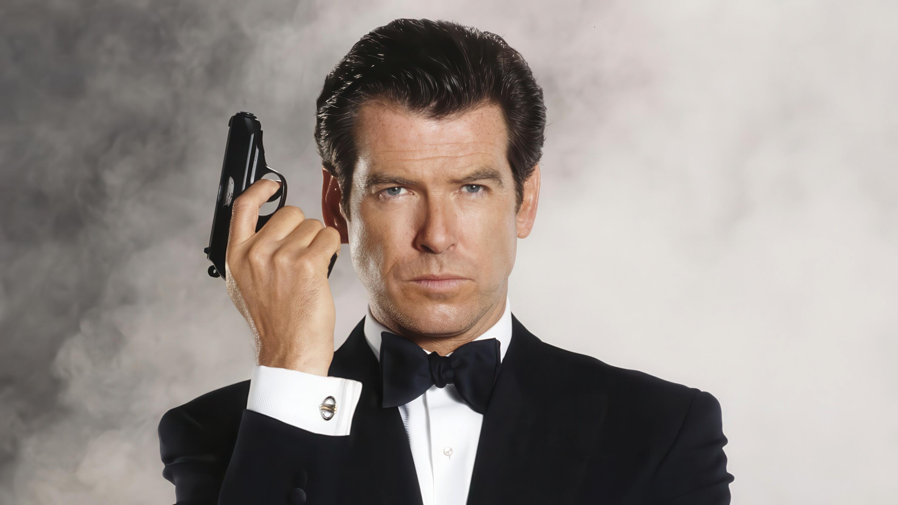 Pierce Brosnan posing in a dark dinner jacket and white shirt as James Bond, 007, for his second EON produced movie, Tomorrow Never Dies. He is holding his iconic weapon – the Walther PPK.