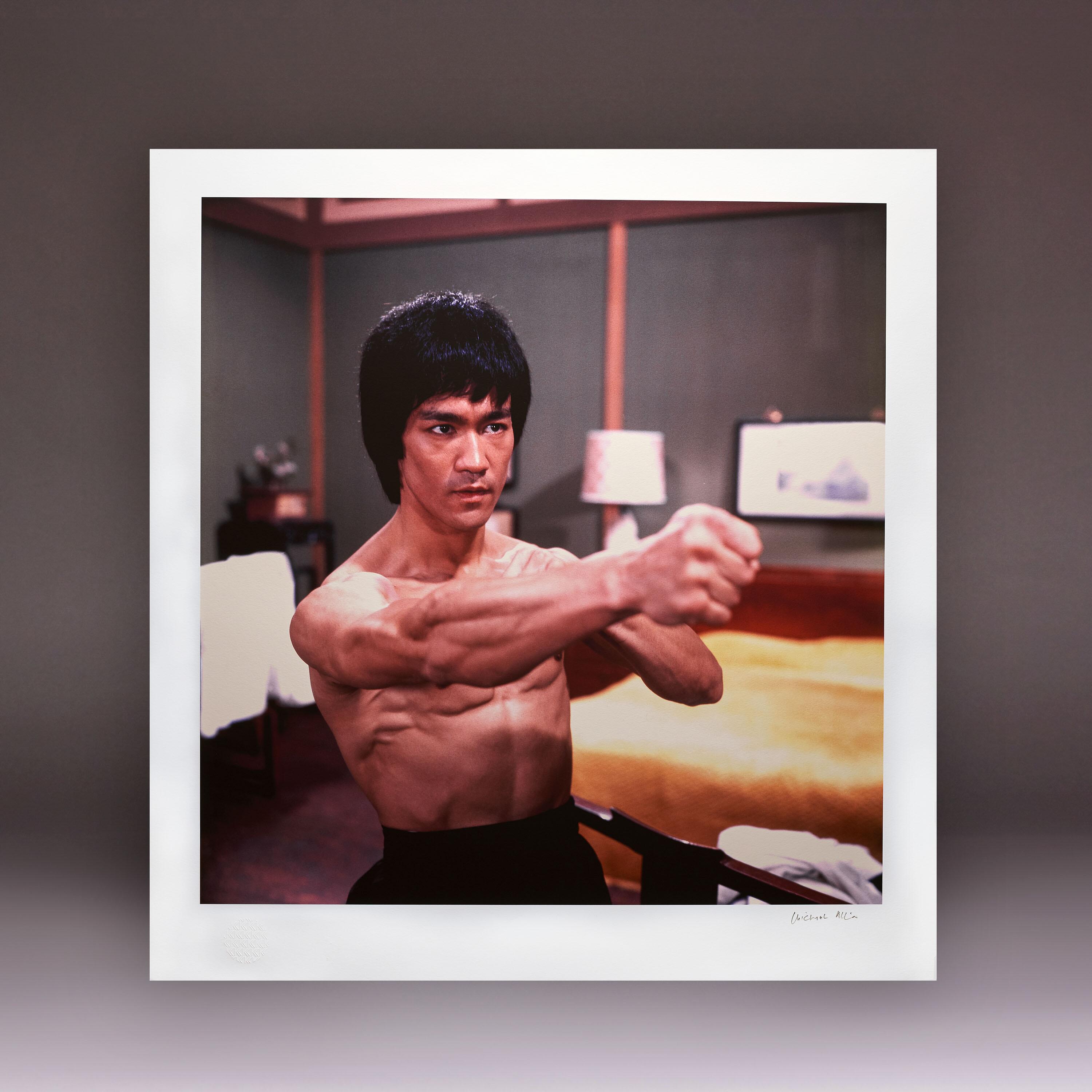 Bruce Lee bare-chested with a prominent muscular fist pose on the Enter the Dragon bedroom set, rare publicity photo.