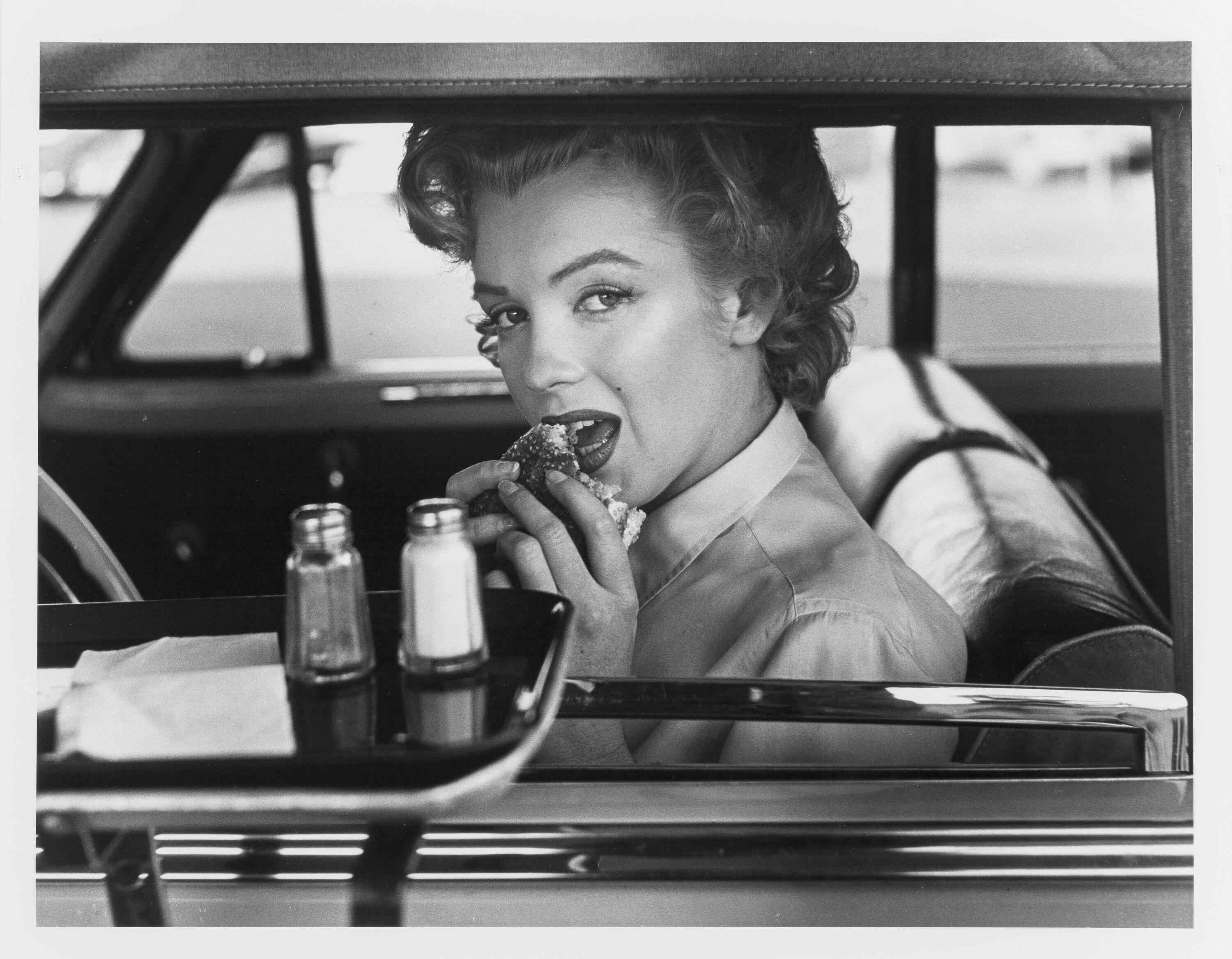 A playful image of Marilyn Monroe eating a burger at a drive-thru