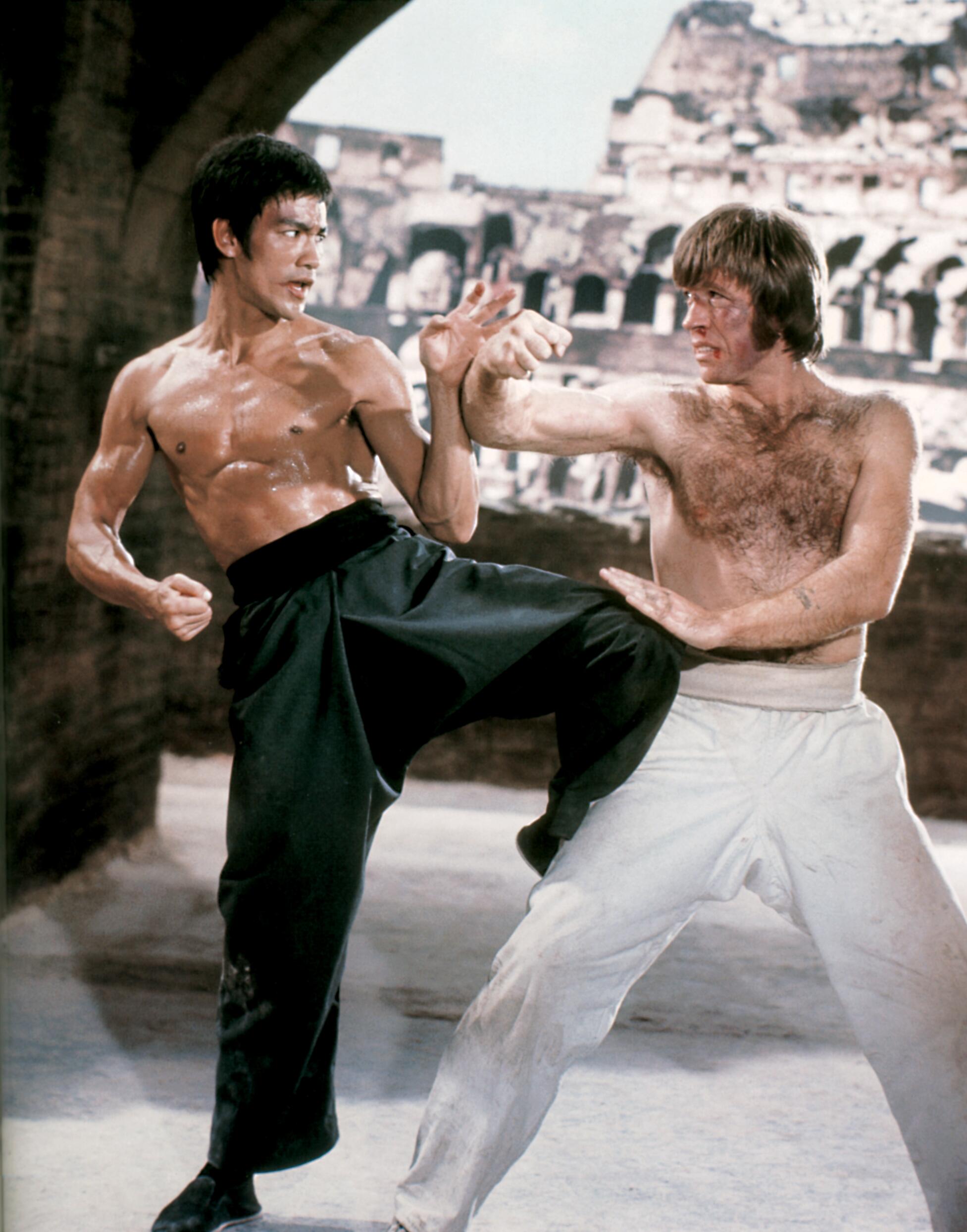 Bruce Lee and Chuck Norris facing off in a famous publicity shot, poised mid stare before their now legendary “gladiator” duel in Rome’s Colosseum for the 1972 martial arts film The Way of the Dragon (Return of the Dragon).