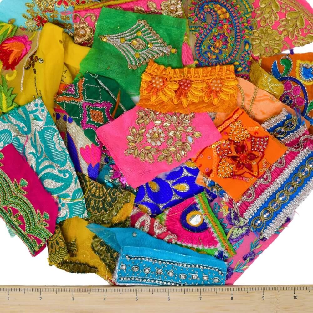 A selection of very small brightly coloured, embellished sari fabric scraps with a wooden ruler placed along the bottom edge