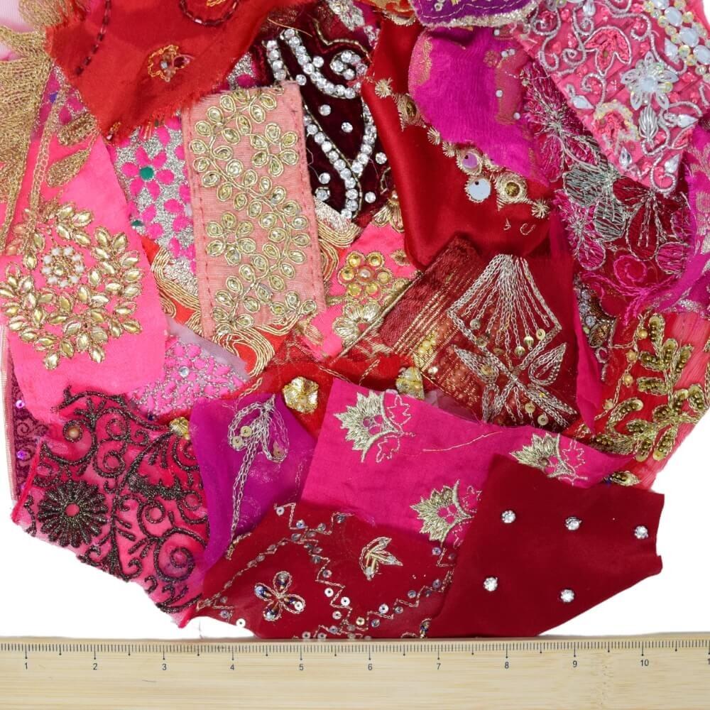 A selection of very small, pink and red embellished sari fabric scraps with a wooden ruler placed along the bottom edge